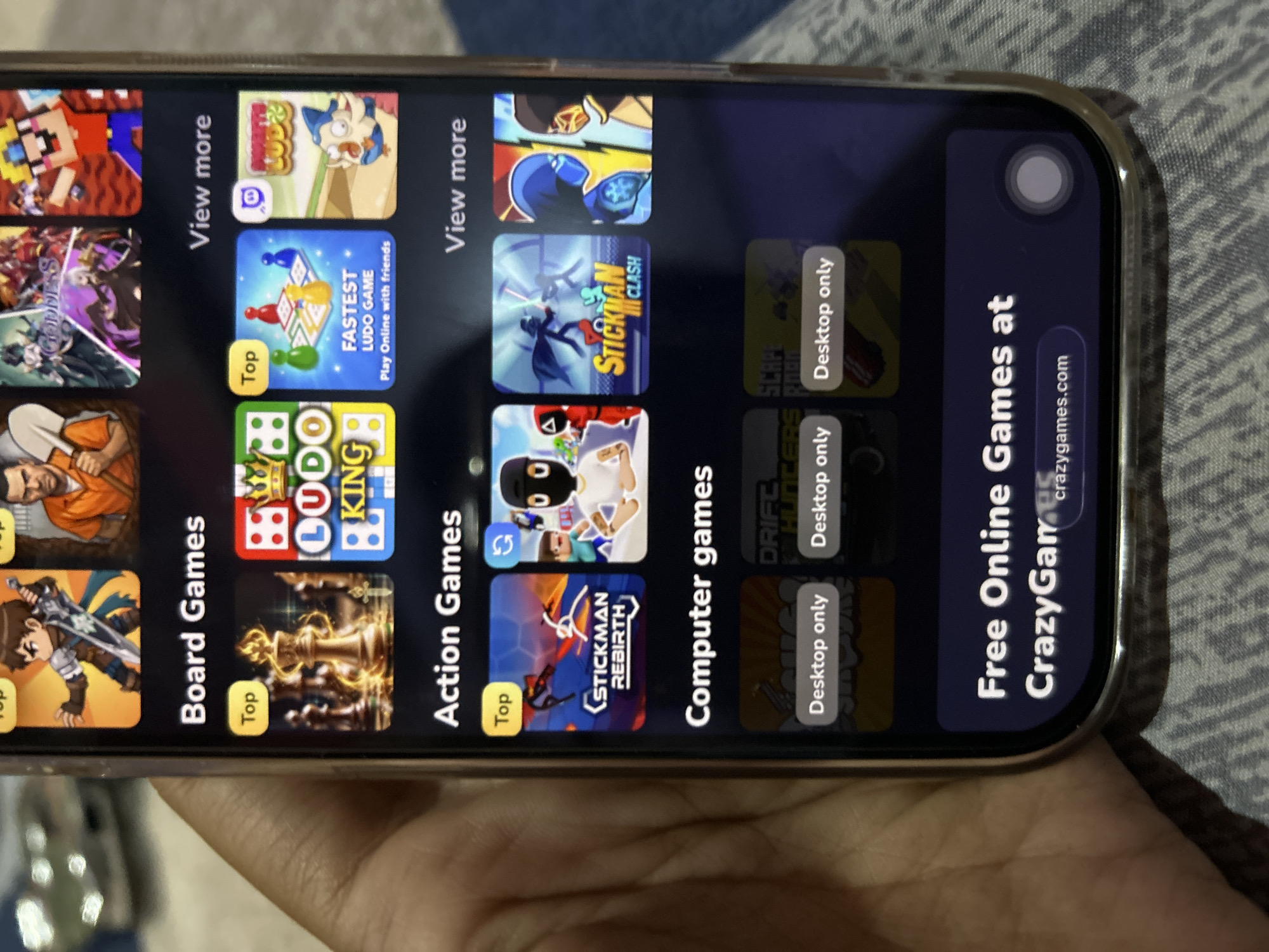 A hand holds a smartphone displaying a game platform interface, with categories like "Board Games," "Action Games," and "Computer games." Featured games include "LUDO KING," "Stickman Rebirth," and "Stickman Clash." At the bottom, a section reads "Free Online Games at CrazyGames.com." The background suggests an indoor setting with a patterned surface. The image does not contain any information related to Depok, Indonesia.