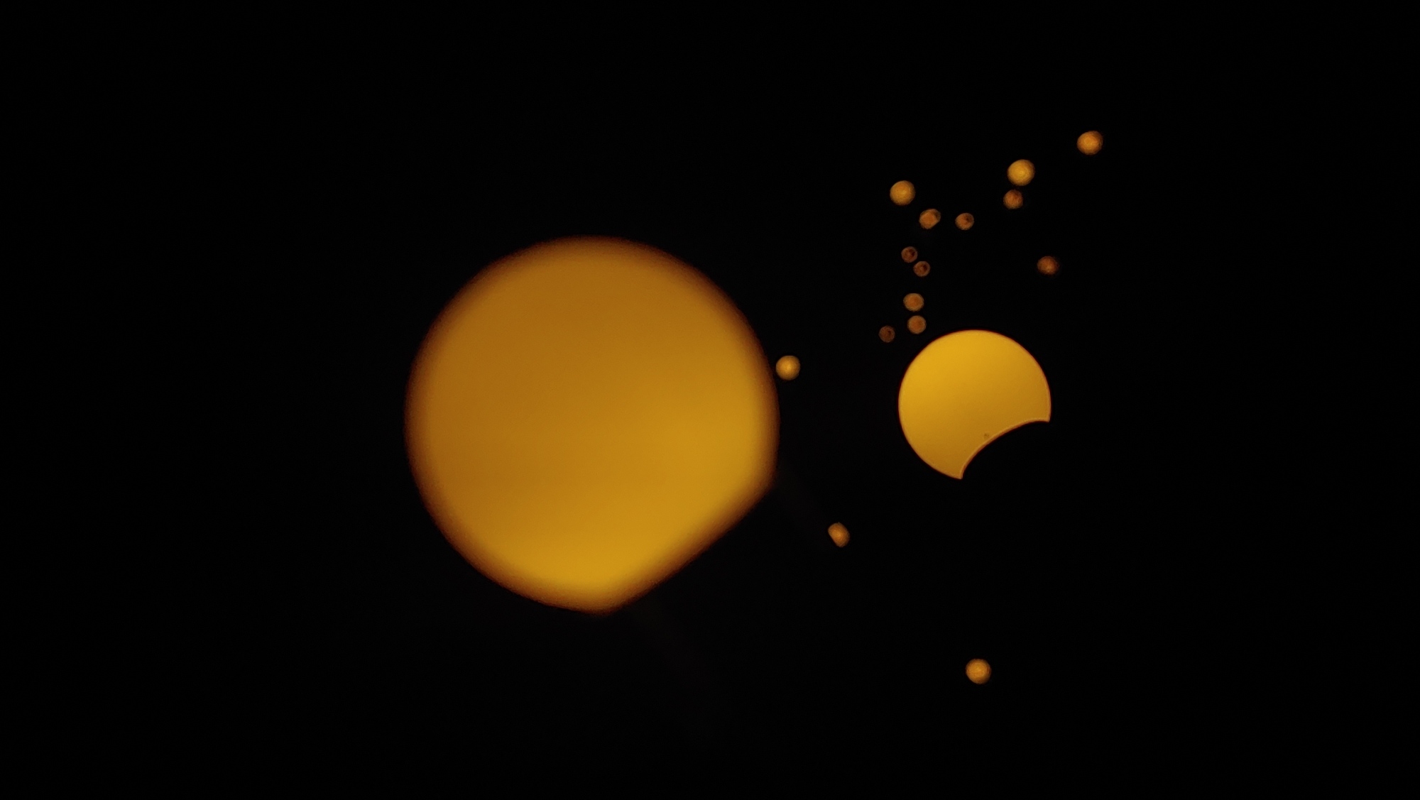 The image depicts a celestial event, likely a solar eclipse, viewed against a dark background. Several circular or crescent-shaped celestial bodies, illuminated in warm yellow and orange tones, are scattered across the frame. One prominent object in the lower center shows a distinct crescent shape, indicating a partial solar eclipse. Other smaller, circular or oval-shaped lights are distributed around it, and a larger, out-of-focus luminous circle is positioned in the upper left quadrant. The overall impression is of a night sky or a very dark environment where these celestial phenomena are visible. The specific location in Mukachevo, Ukraine, cannot be determined from the visual information in the image.