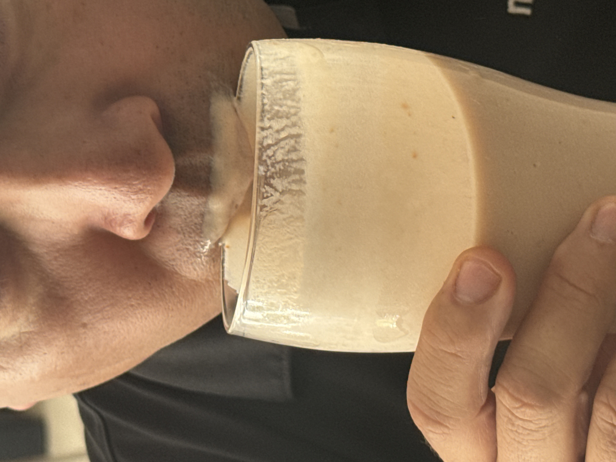 A person is drinking from a glass. The glass contains a tan liquid. The person's hand is holding the glass. The scene does not provide enough detail to determine the location of the photograph within the city of Santa Clara Ocoyucan, Mexico.