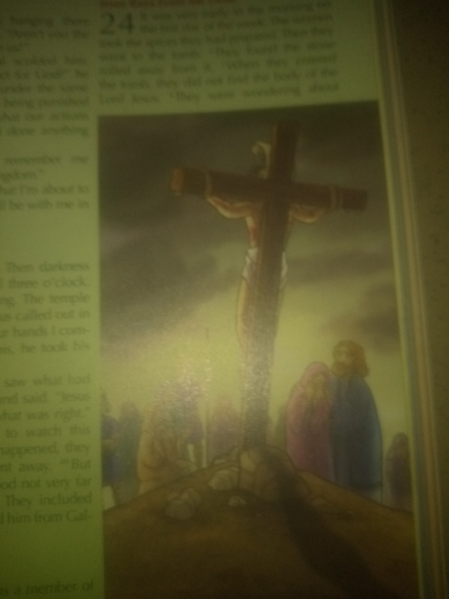 The image depicts a biblical scene featuring a crucifix with a figure of Jesus. The background is blurred and appears to be a landscape with a cloudy sky. There are several figures of people standing around the base of the crucifix. The scene is presented in a muted, earthy color palette. The text to the left of the image appears to be from a religious book. The image is likely a print or a page from a book, with a slightly out-of-focus quality. There is no information within the image itself or the provided crops that specifies a location in Jauro Yinu, Nigeria.