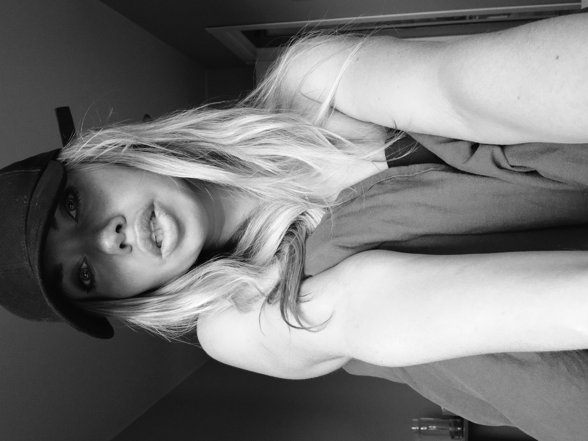 A grayscale portrait of a woman wearing a baseball cap is presented. She is fair-skinned and has long, wavy hair. Her lips are slightly parted in a smile. The setting appears to be indoors, with a plain wall in the background. There is no evidence in the image to indicate the location is in Votkinsk, Russia, or to provide any specific forensic details about the scene, actions, or interactions.