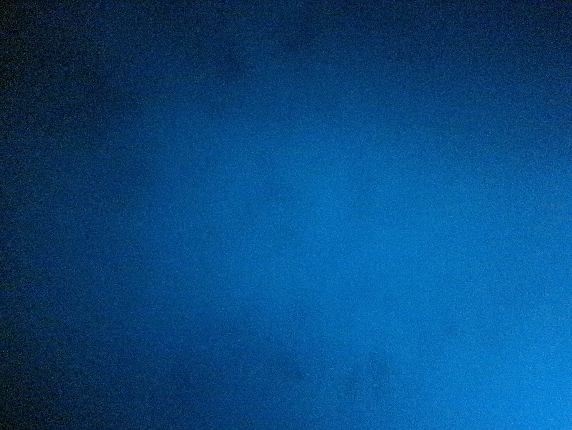 The image is a slightly grainy, close-up shot of a solid, gradated blue surface. The blue is darker in the upper left corner and gradually lightens towards the lower right corner. There are no discernible objects, people, or environmental details visible. No connection to the city of Razgrad, Bulgaria, is evident.