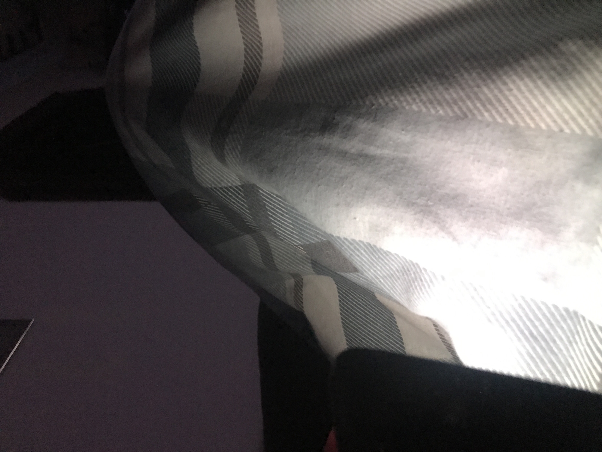 The image shows a close-up of bedding with a striped pattern. The bedding is mostly white with gray stripes. The surrounding environment appears dark, with a glimpse of a dark surface possibly a bedside table. The quality of the image is somewhat grainy. No people are visible. There is no information available to identify the location as Yerevan, Armenia.