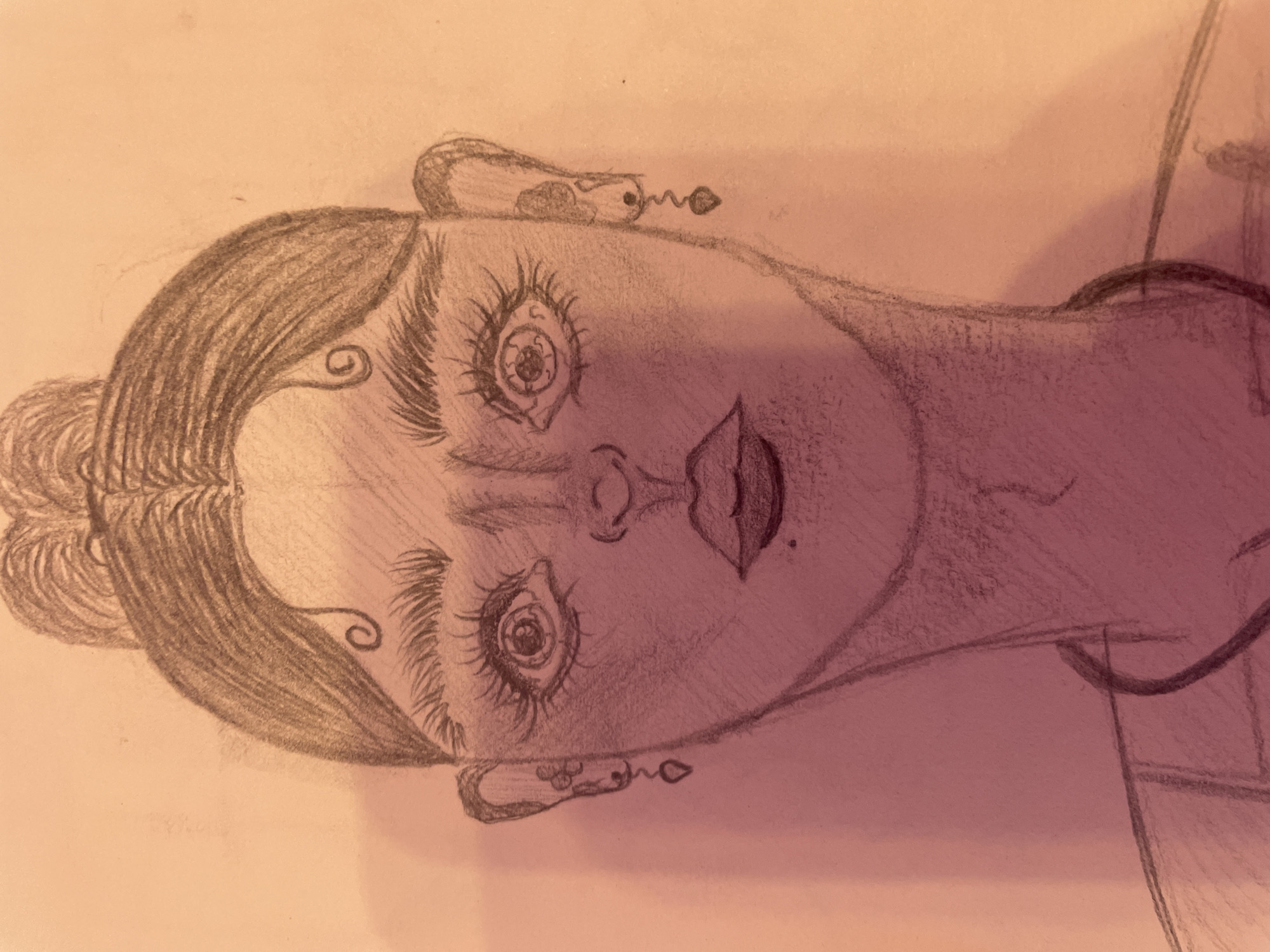 The image is a black and white pencil sketch of a young woman's face. She has her hair pulled up in a bun with a few wisps framing her forehead. Her eyes are large and wide, with prominent eyelashes. She has high cheekbones, a small nose, and full lips. She is wearing earrings that appear to be teardrop-shaped. The sketch is rendered with heavy shading, giving it a somewhat dramatic and stylized appearance. The background is blank, suggesting it is a portrait. There is no indication of the location in Sinyavino, Russia, or any other specific setting.