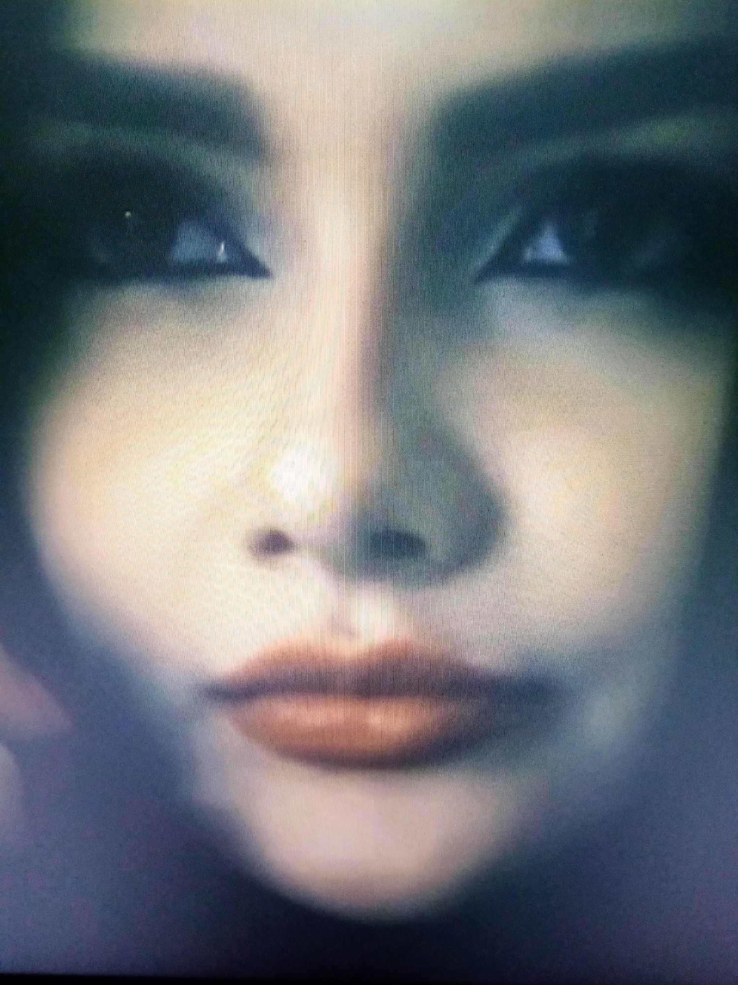 This is a close-up, slightly blurry media file of a person's face, focusing on their eyes and lips. The lighting is dim and appears to be artificial, possibly from a screen, casting a diffused glow on the skin. The subject has dark eye makeup and reddish-brown lipstick. The background is dark and out of focus, providing no contextual information about the setting. There are no visible objects, text, or indications of the time of day, weather, or specific location within Chirakchi, Uzbekistan. The overall mood is somewhat enigmatic due to the blurriness and close cropping.