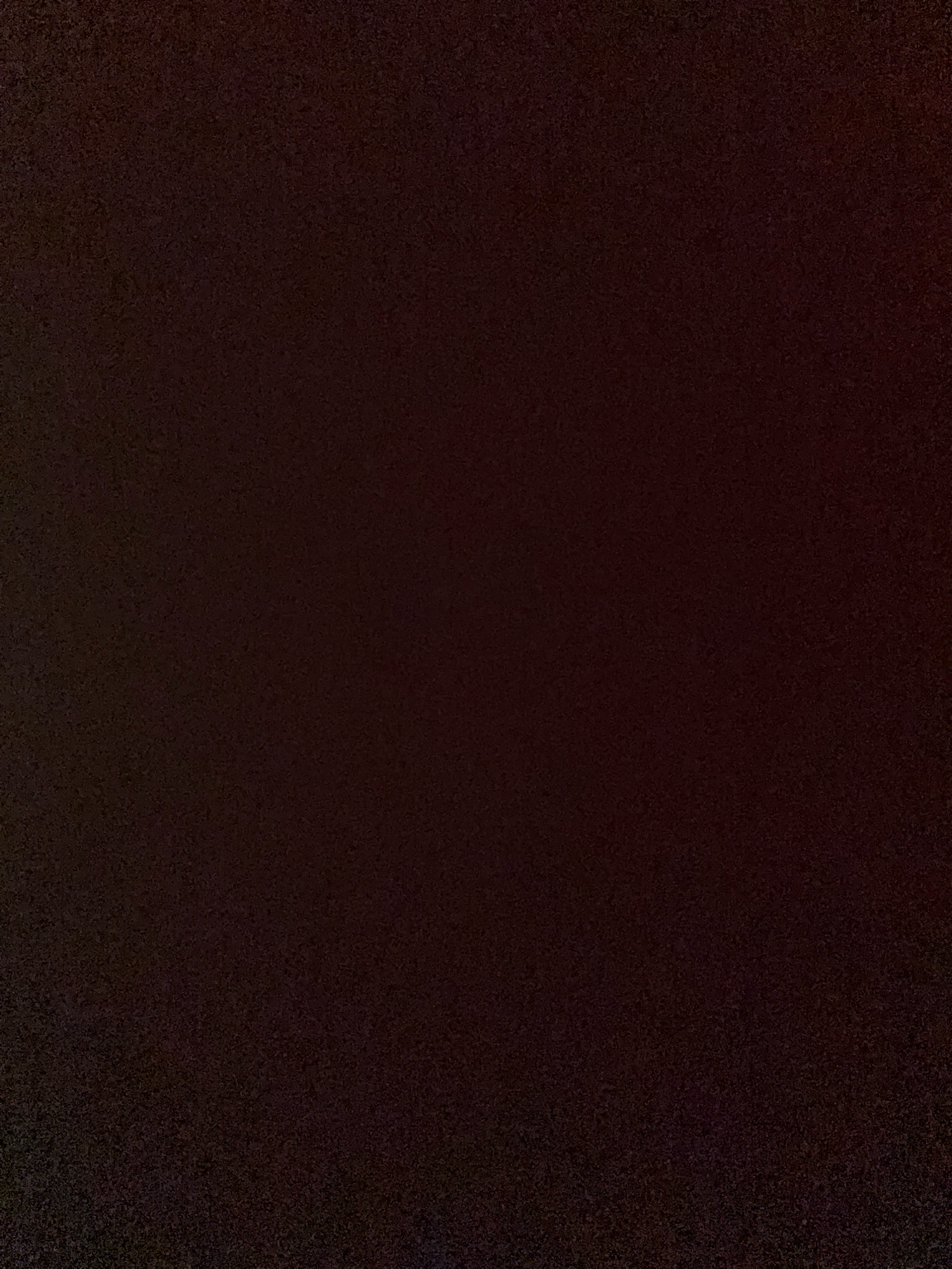 This is a photograph of a dark, textured surface. The color is a very deep, almost black, shade of brown or maroon. The texture appears to be granular or speckled, with subtle variations in shade that suggest a rough or uneven material. There are no discernable objects, people, or environmental features visible in the image, making it an abstract composition of color and texture. The image provides no information about its location in Howrah, India, or any other specific context.