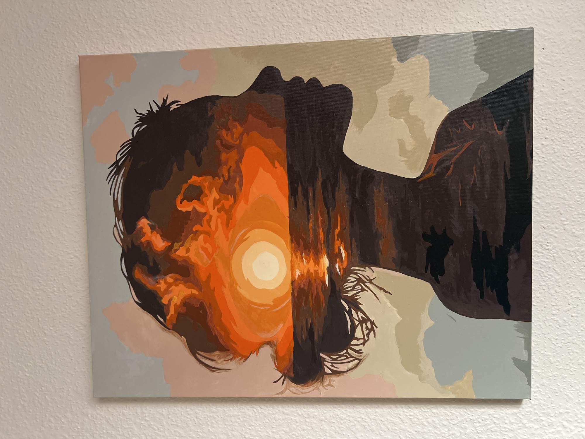 A painting of a woman's profile is shown, with a sunset over the ocean filling her silhouette. The woman's profile is dark, with the sunset colors of orange, yellow, and red visible within. The ocean is dark, reflecting the sunset. The background of the painting is a light sky with clouds in shades of pink and gray. The painting is hanging on a white textured wall.