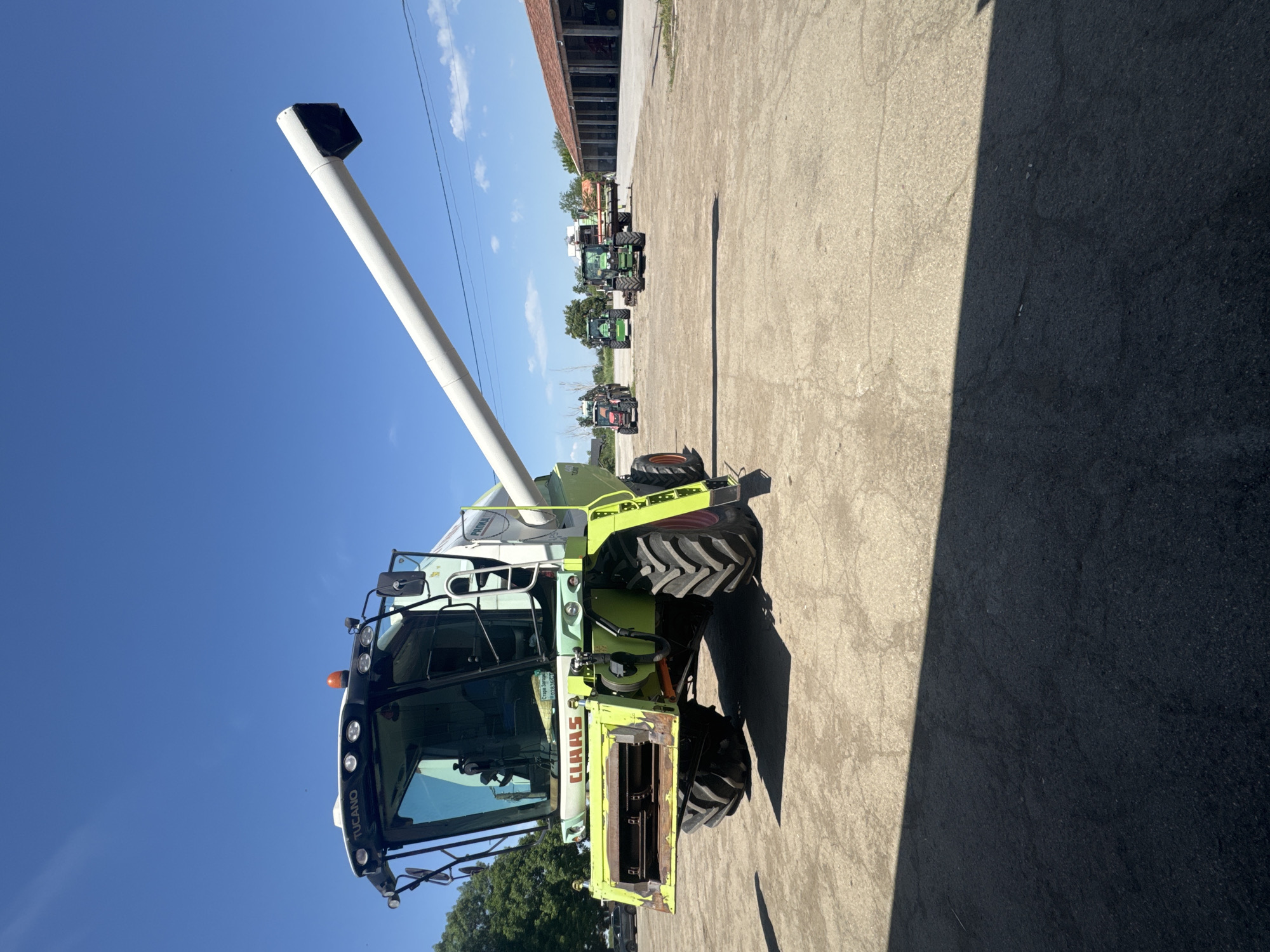 The image depicts a light green Claas Tucano combine harvester parked on a concrete surface under a clear blue sky. Several tractors are parked in a row behind the combine. The scene appears to be outdoors. "TUCANO" is labeled across the front of the tractor. The specific location in Sarnevo, Bulgaria, is not discernable from the image. There are no visible people.