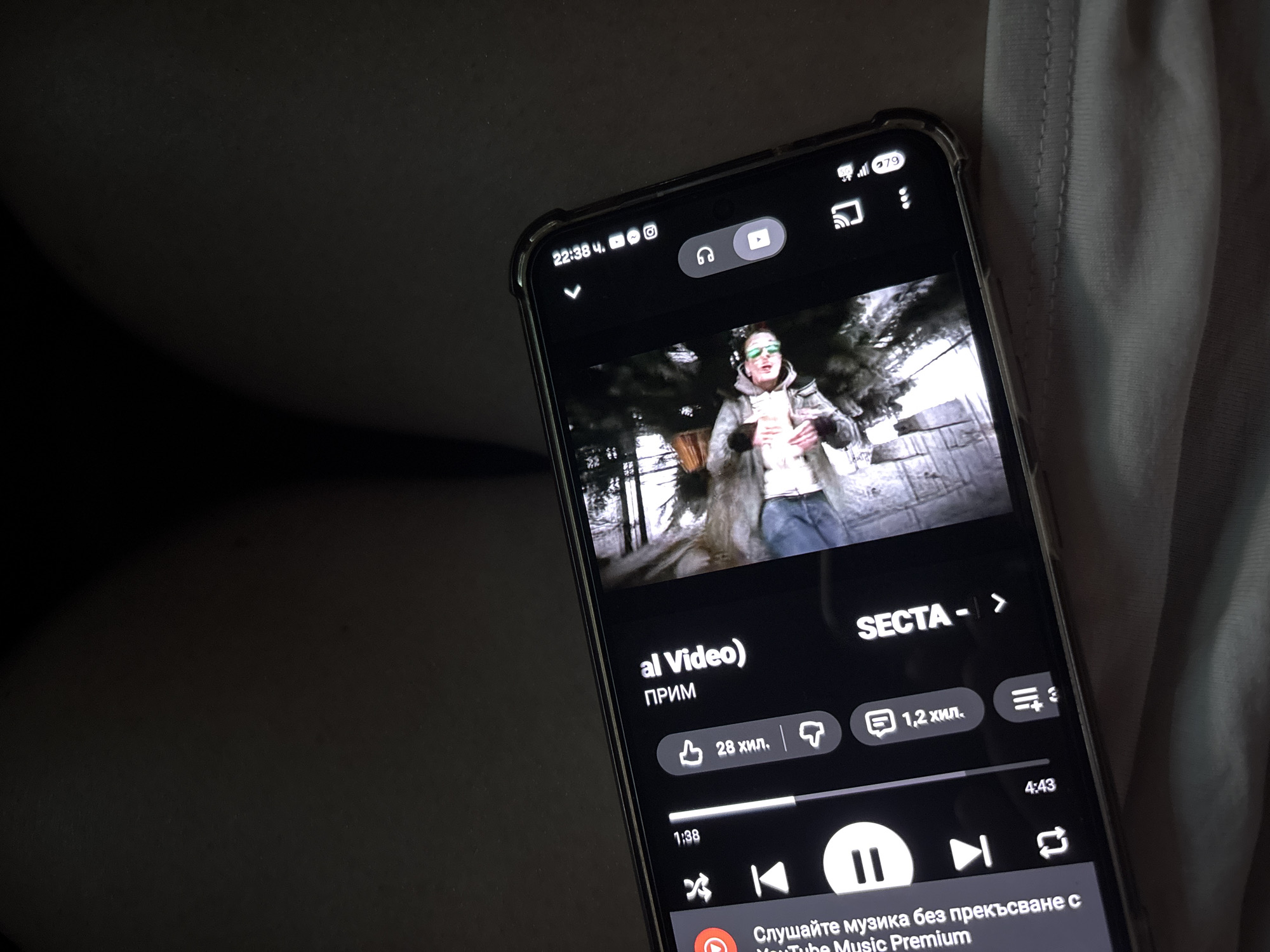 A smartphone is showing a YouTube Music video with the title "SECTA" by PRIM, located in Koprivlen, Bulgaria. The video's name is "al Video)". The video has 28,000 likes and 1,200 comments. The video is 1 minute and 38 seconds into a 4 minute and 43 second duration. The phone's screen shows it is 22:38 and has a battery level of 79%.