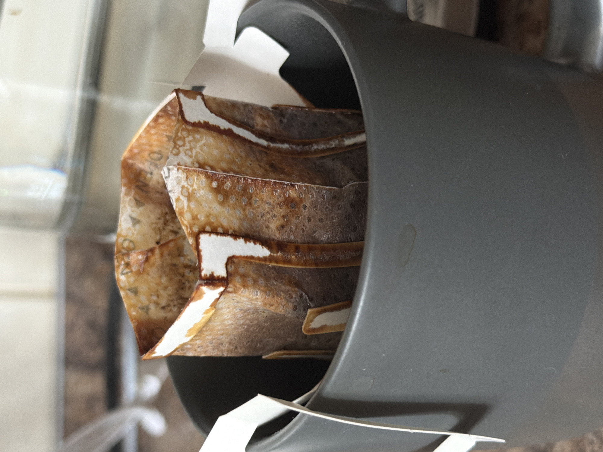 A close-up shot shows a gray kitchen appliance containing used coffee filter bags. The filters are brown and damp, with visible coffee residue. The setting appears to be a kitchen, possibly in Khimki, Russia, but without further context, this cannot be confirmed. There are no people visible in the frame.