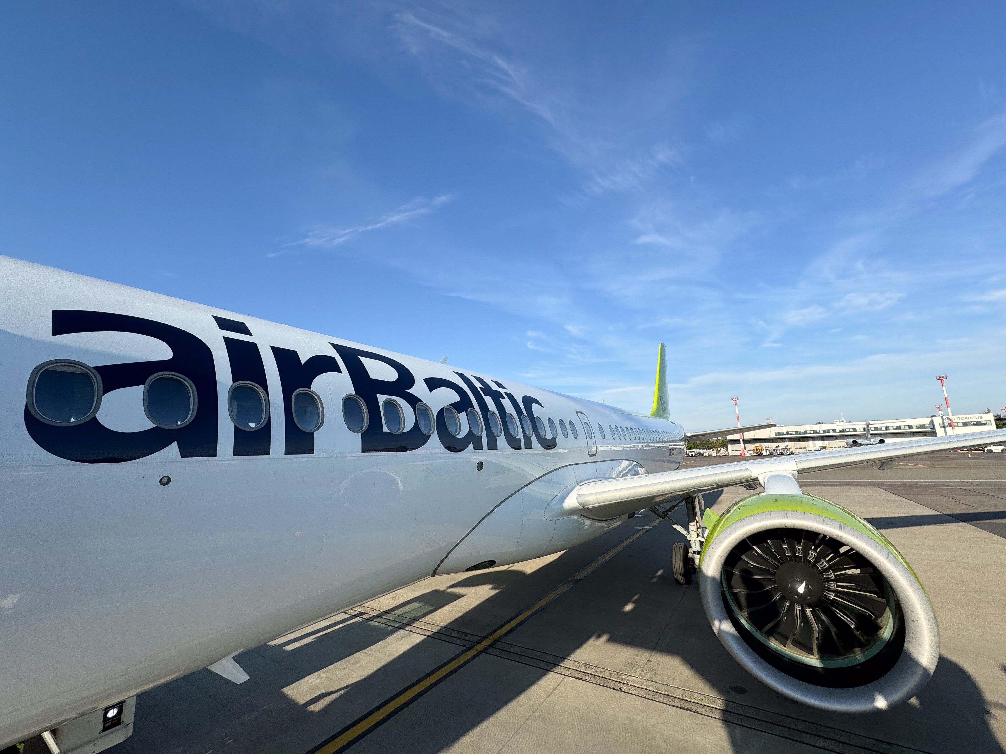 Nahaufnahme eines AirBaltic-Flugzeugs, das bei klarem blauem Himmel auf dem Rollfeld parkt.