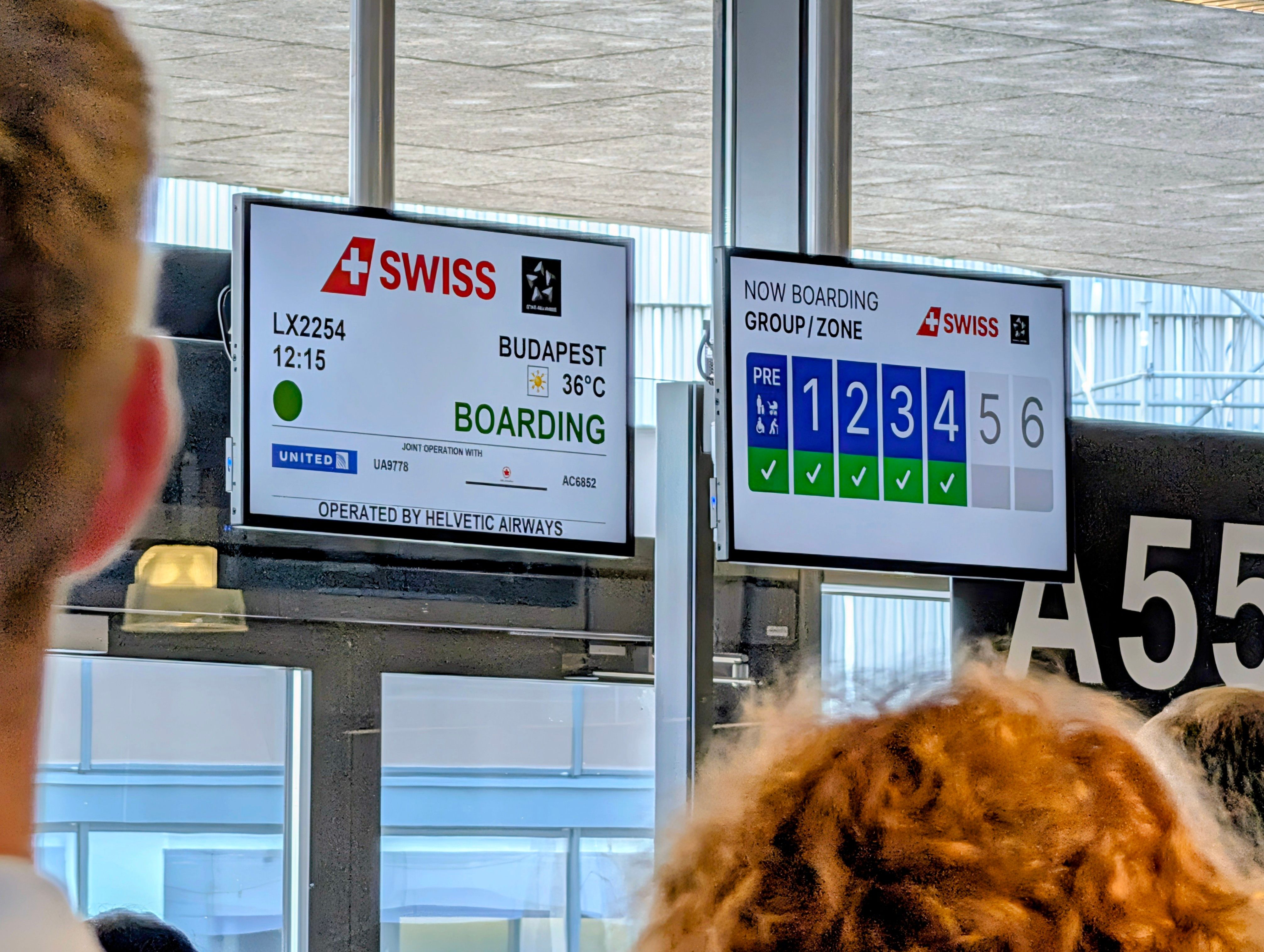 Passagiere warten am Gate auf Boarding für SWISS Flug nach Budapest. Digitale Anzeigen zeigen Gruppen 1-4 im Boarding.