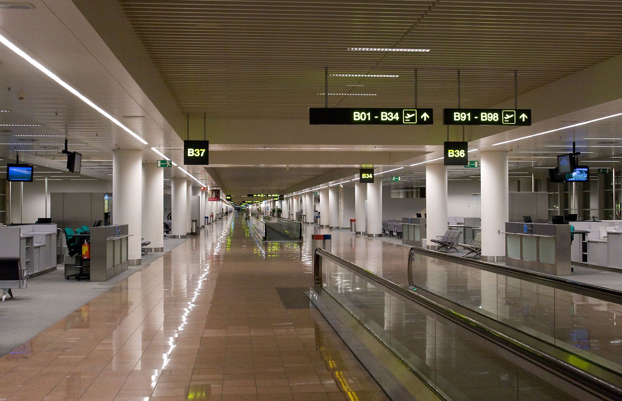 Leerer Flughafenterminalflur mit Laufband und Flugsteigbeschilderung.