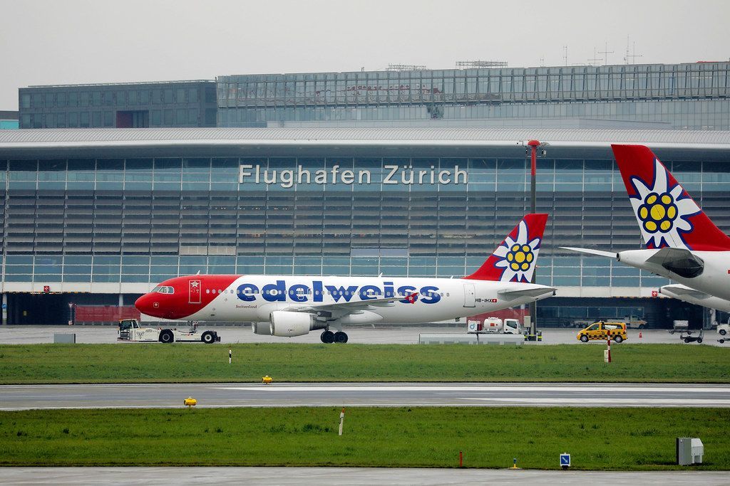 Edelweiss Air Flugzeug am Flughafen Zürich mit Flughafengebäude im Hintergrund.