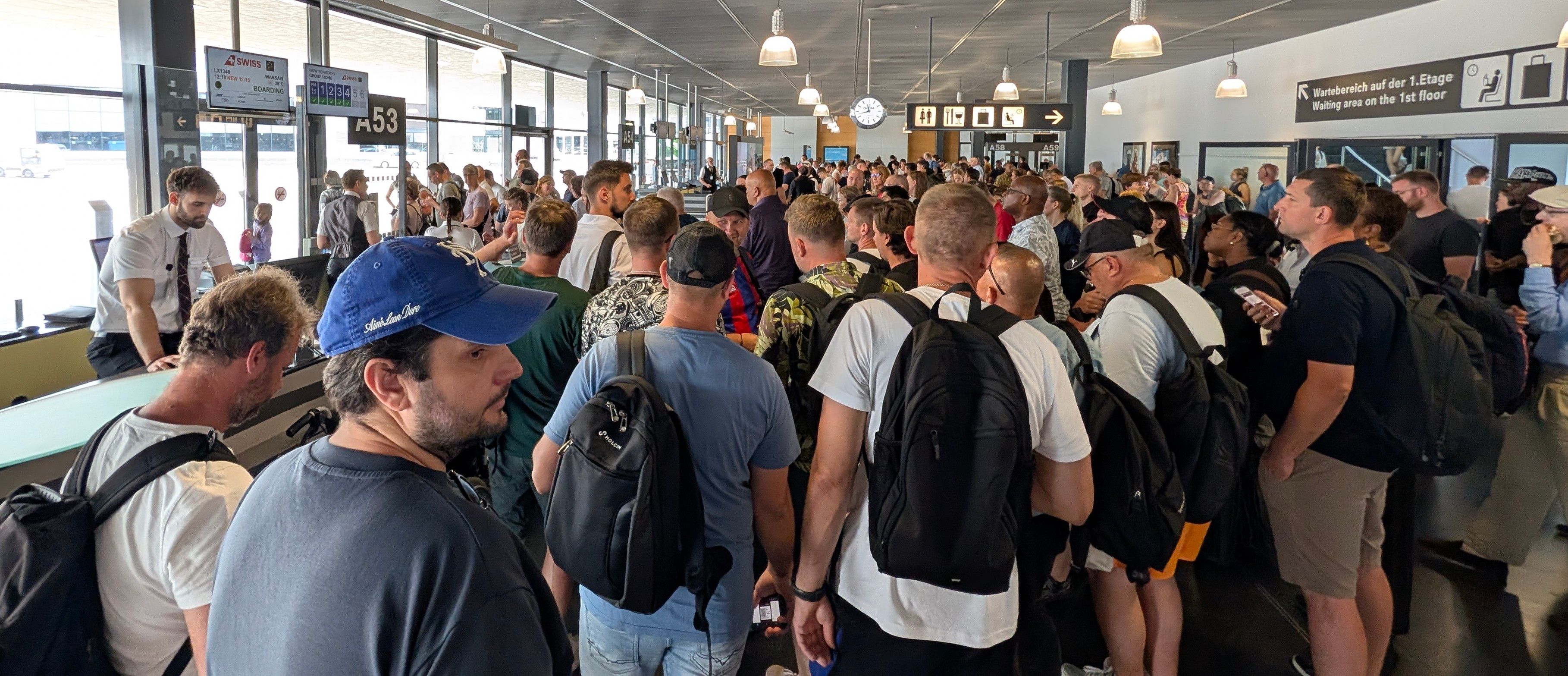 Ein überfülltes Flughafengate mit vielen Passagieren und Rucksäcken, die auf einen SWISS-Flug nach Warschau warten.