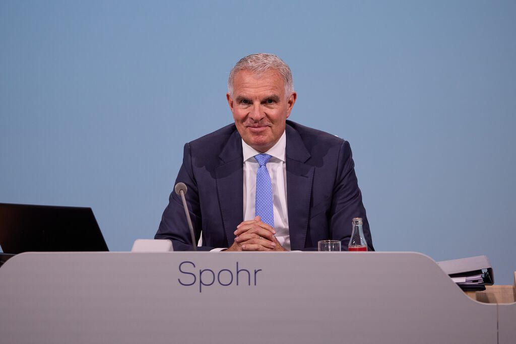 Lufthansa CEO Carsten Spohr sitting at a press conference table with a nameplate, looking towards the camera.