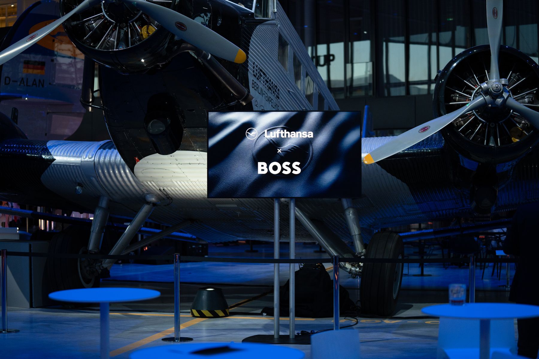 Eine Ankündigung der Lufthansa x BOSS Partnerschaft vor einem historischen Junkers Ju 52 Flugzeug.