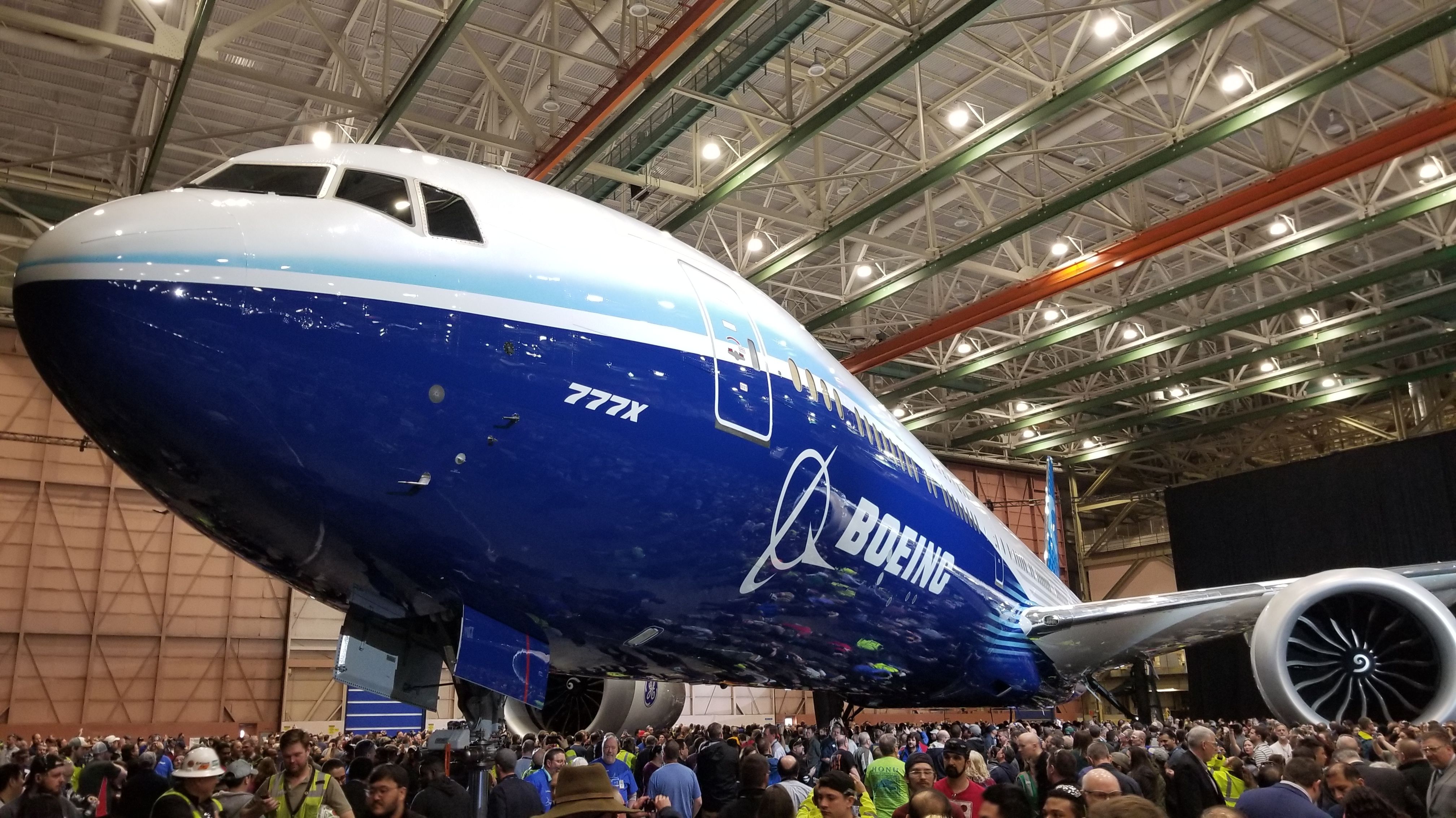 Das neue blau-weiße Boeing 777X Flugzeug wird in einem Hangar vor einer großen Menschenmenge präsentiert.