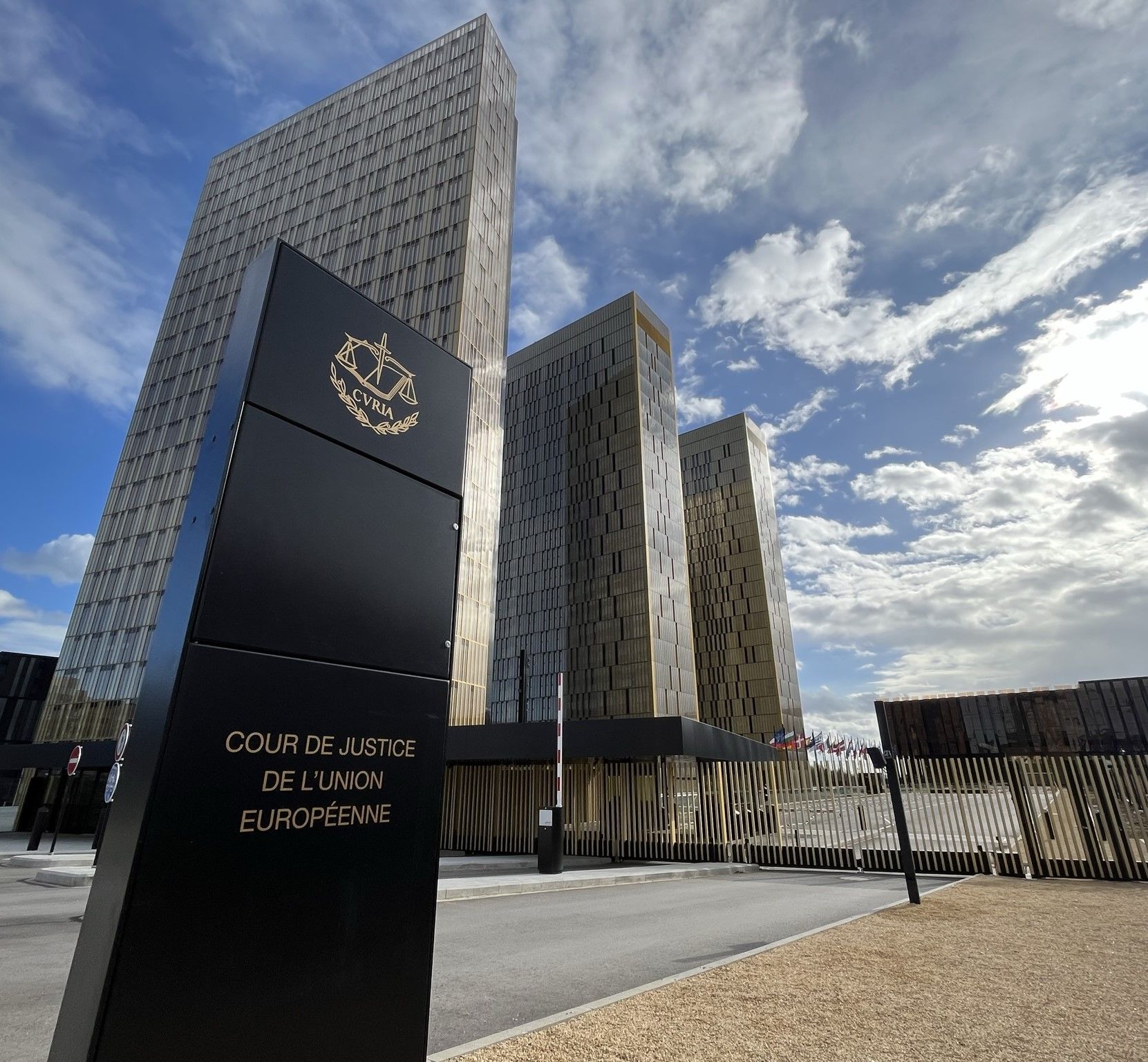 Hauptsitz des Europäischen Gerichtshofs in Luxemburg mit den markanten gläsernen Zwillingstürmen und dem Eingangsschild unter blauem Himmel.