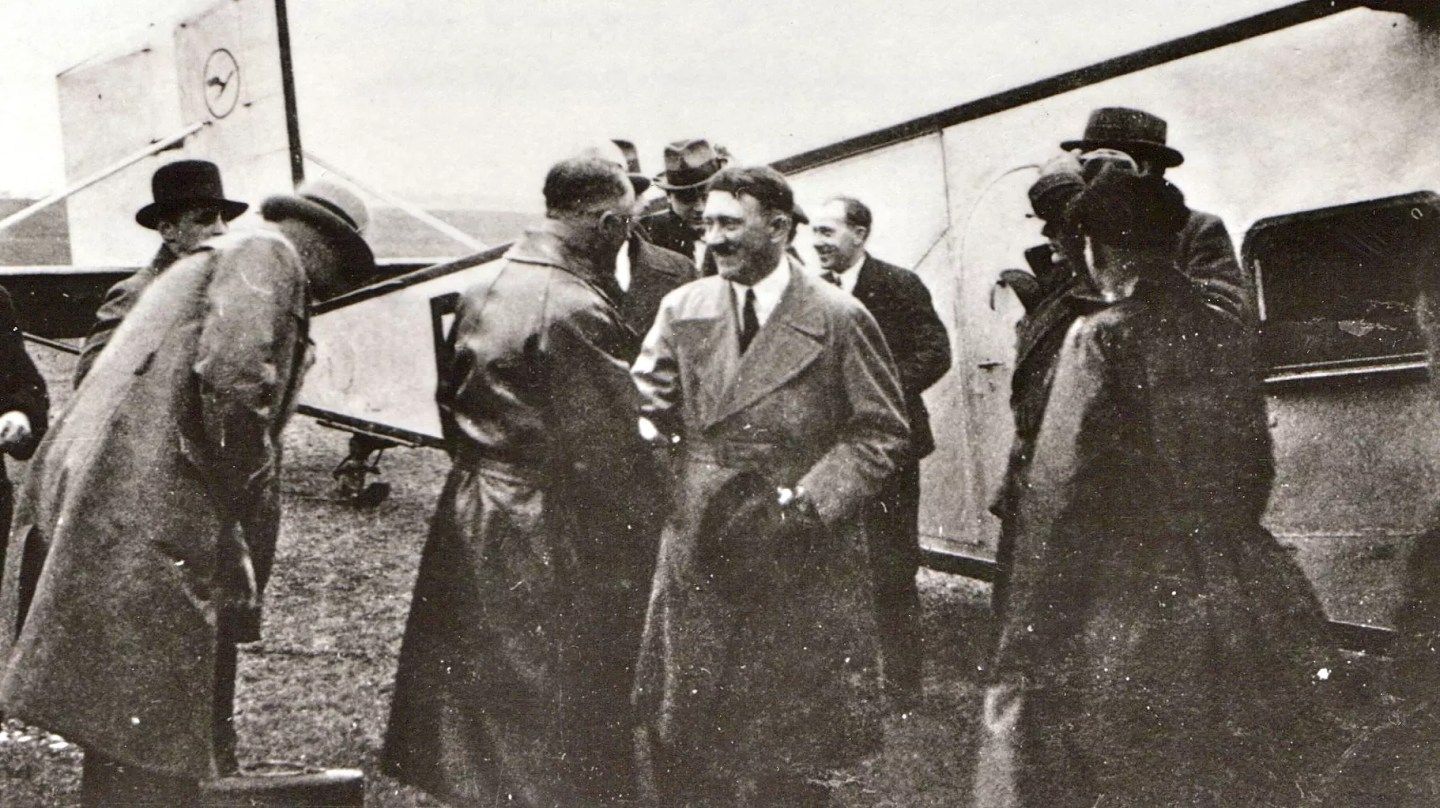 Adolf Hitler schüttelt Hände vor einem Lufthansa-Flugzeug.