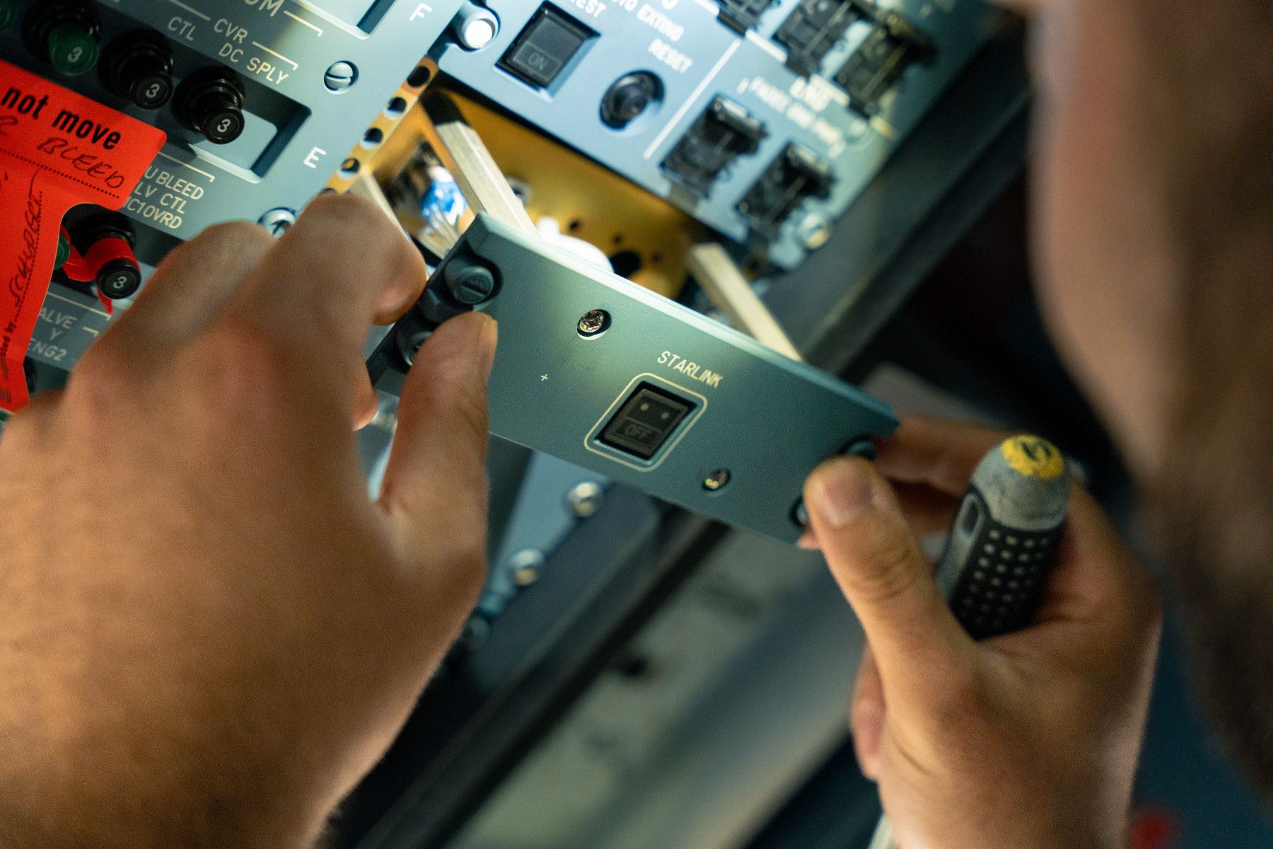 A technician installs a Starlink component with an 'OFF' switch into an aircraft's overhead panel.