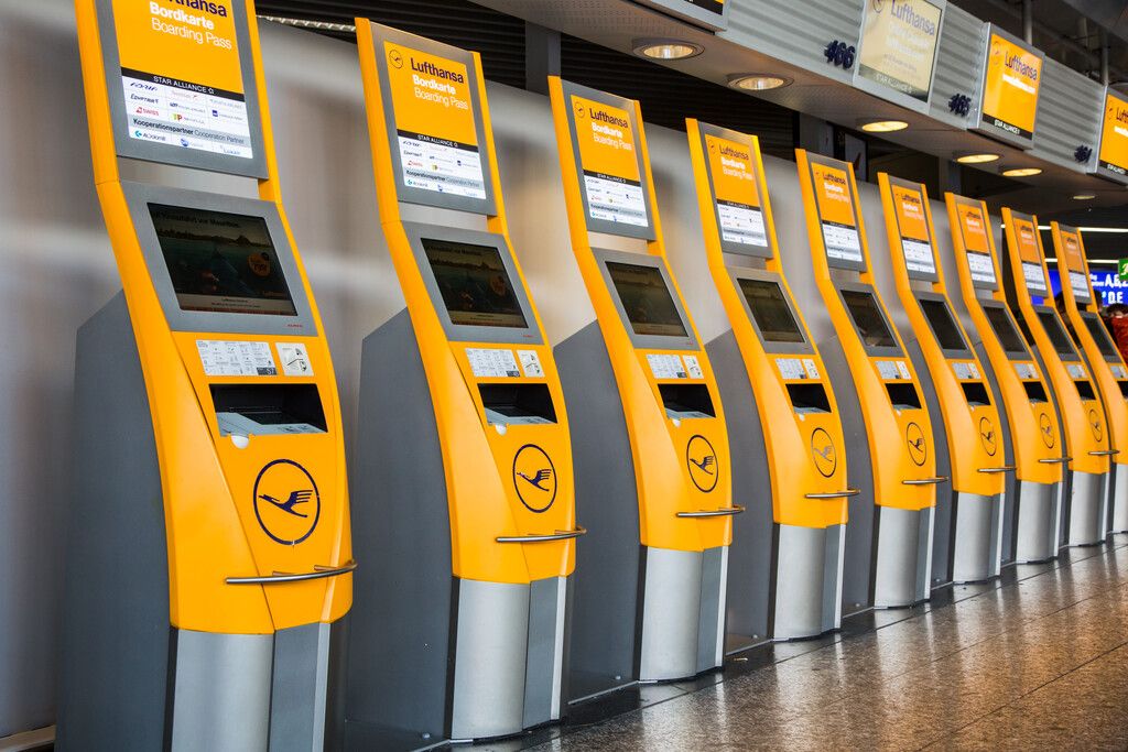 Eine Reihe gelber Lufthansa-Check-in-Automaten an einem Flughafen-Terminal.