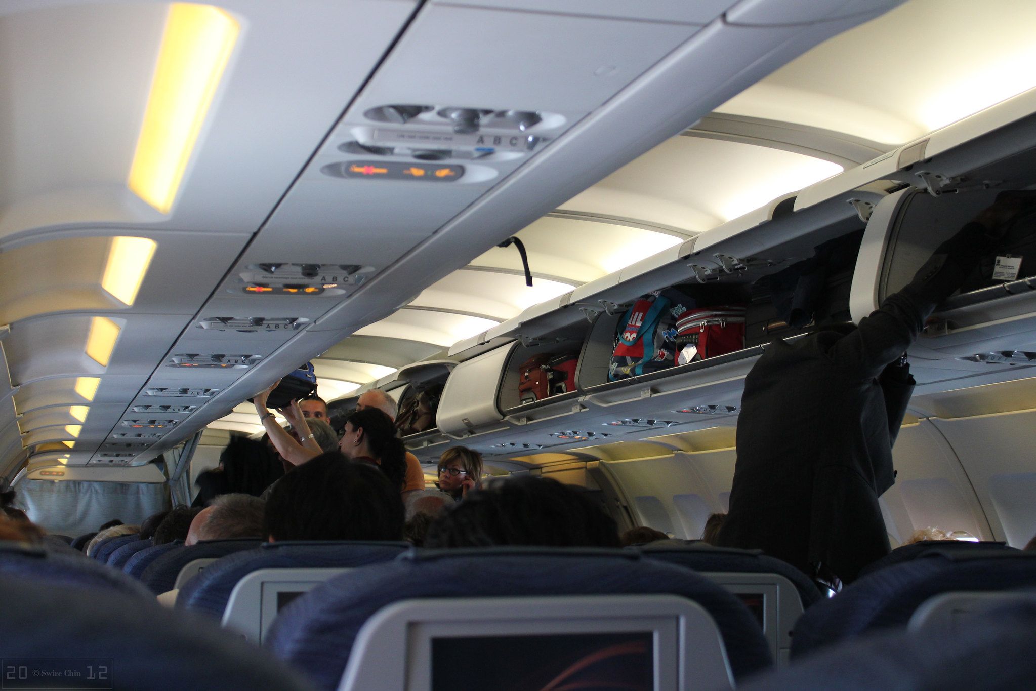 Passagiere, die versuchen, ihr Handgepäck in den überfüllten Gepäckfächern eines Flugzeugs unterzubringen.