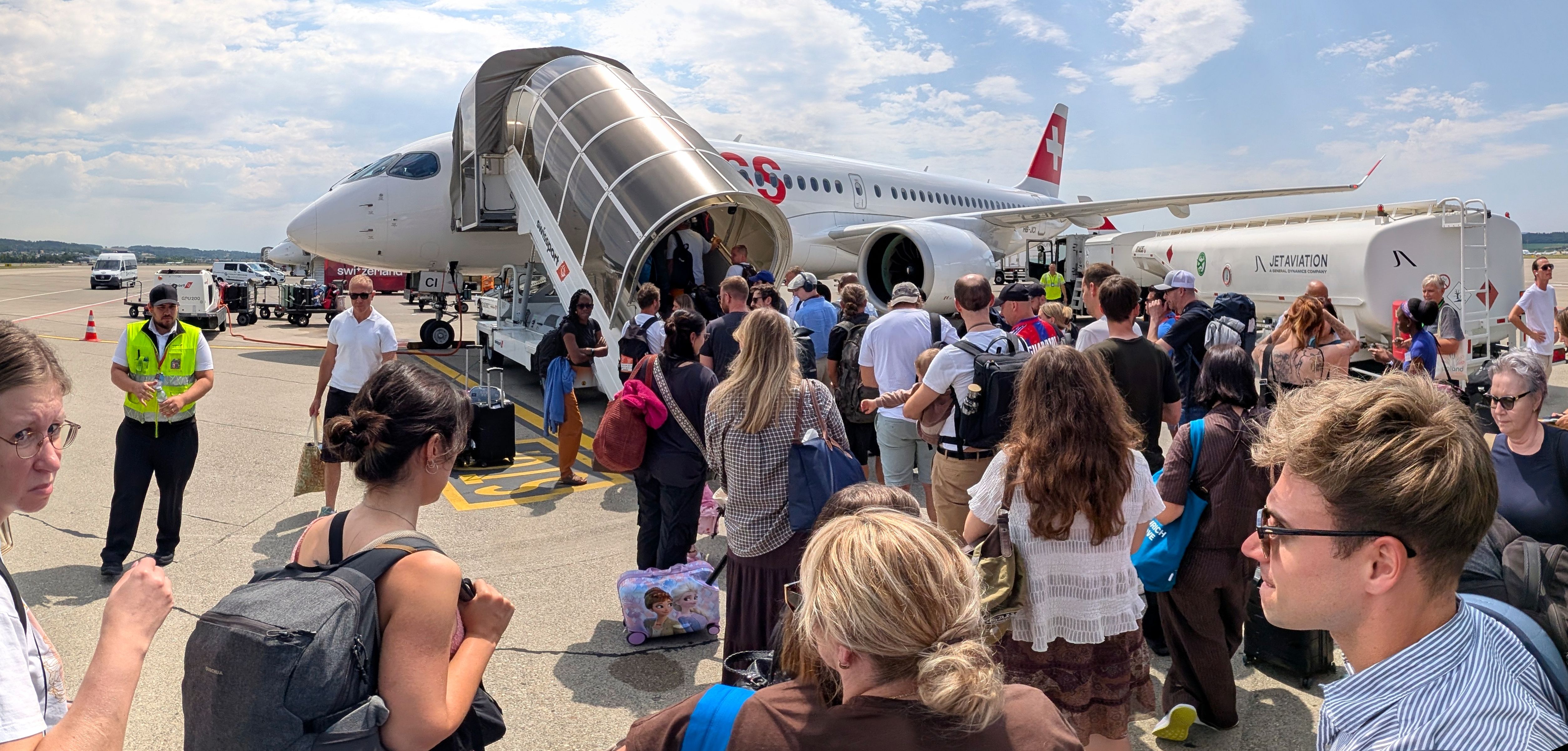 Passagiere besteigen ein Flugzeug der Swiss International Air Lines auf dem Rollfeld über mobile Treppen, mit Bodenpersonal.