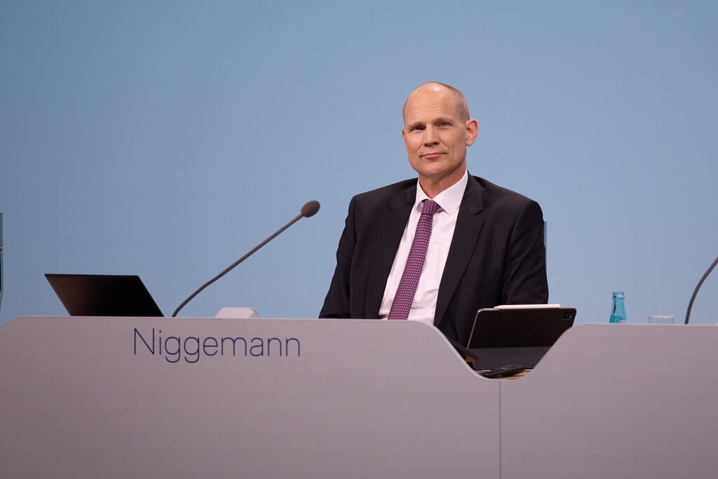 Lufthansa-Manager Frank Niggemann sitzt an einem Konferenztisch vor einem hellblauen Hintergrund.