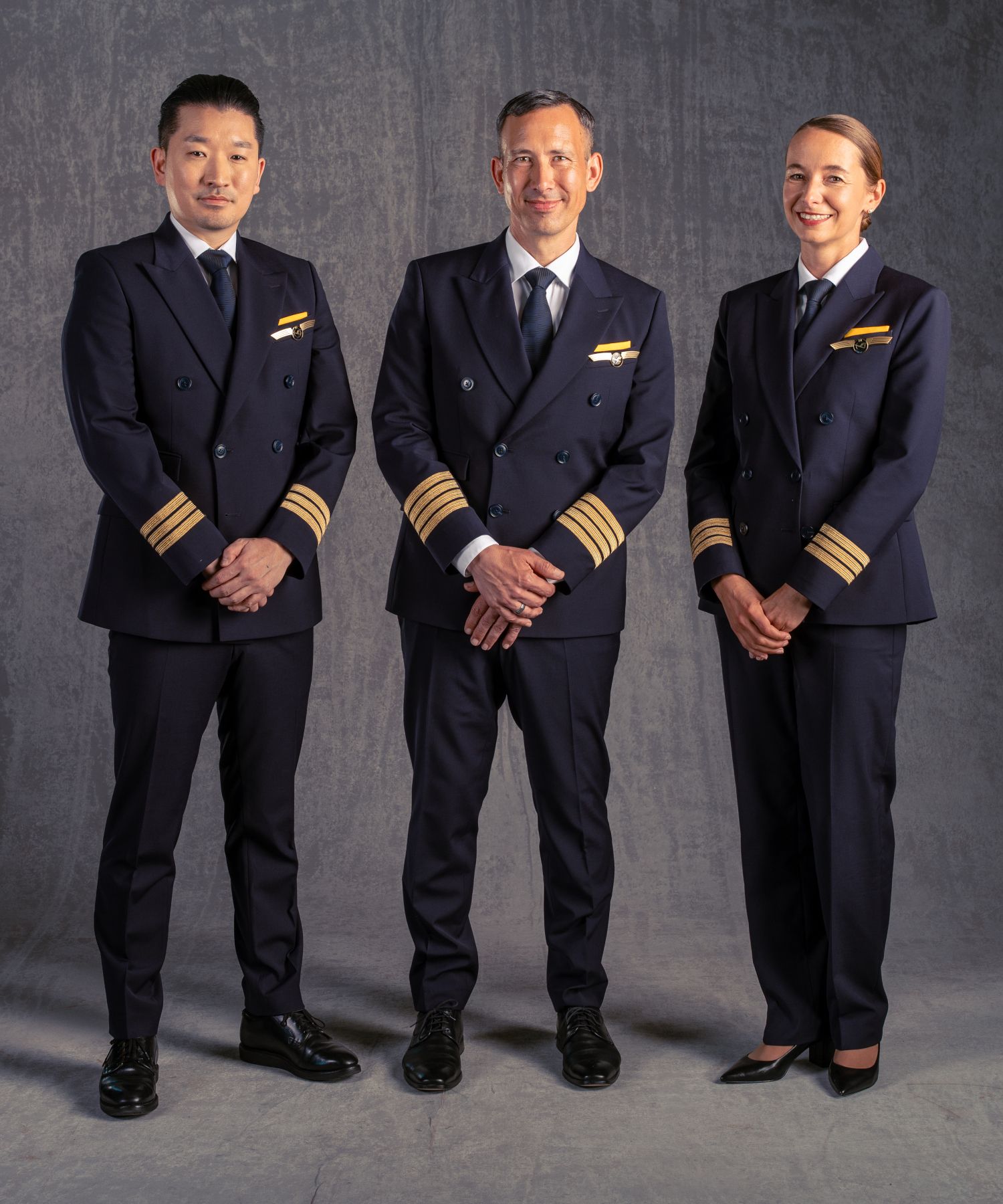 Drei Lufthansa-Piloten in neuen, von BOSS entworfenen Uniformen vor neutralem grauem Hintergrund.