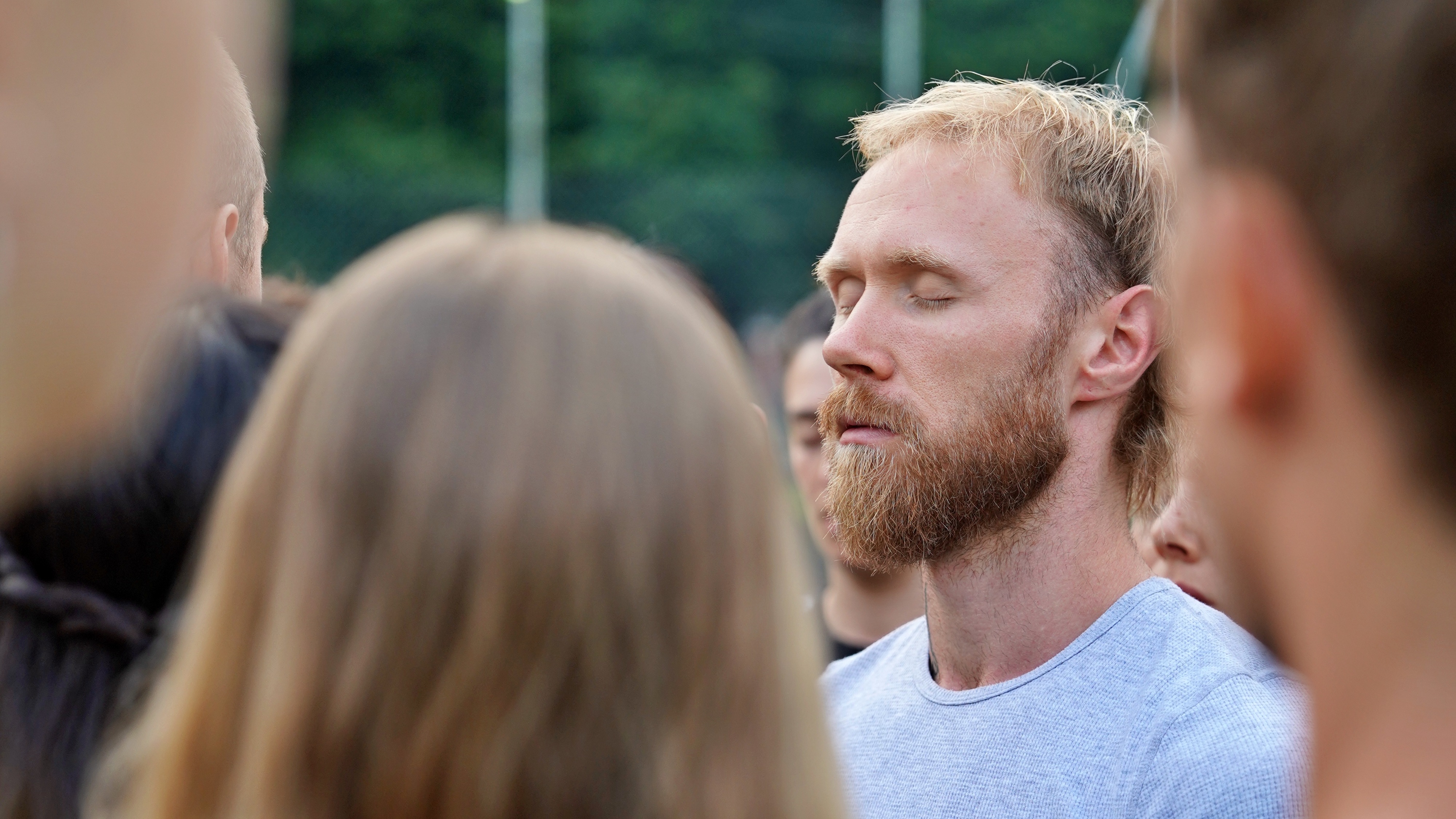 A bearded man with his eyes closed, standing in a group outdoors during a mindfulness session