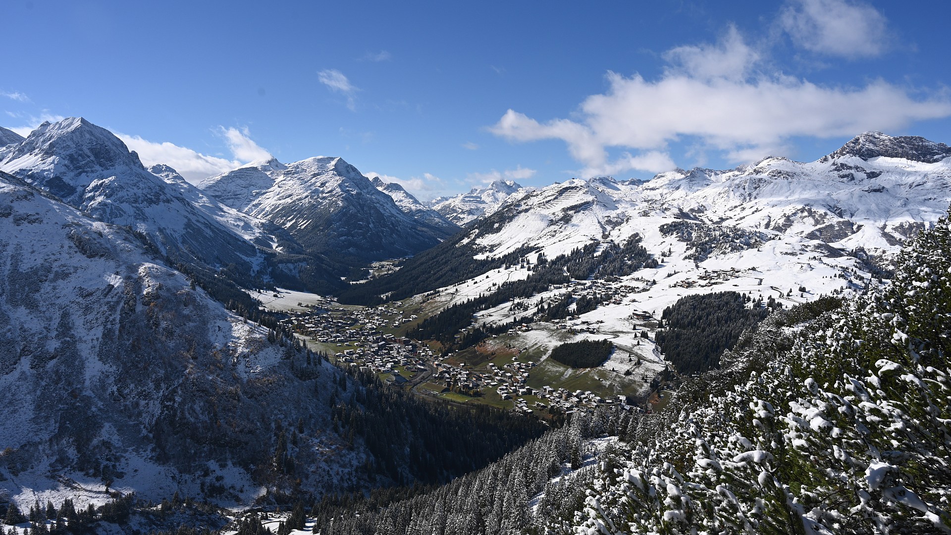 Lech am Arlberg on 22 October 2026 at 13:00: fresh snow on the village, the slopes and the peaks under a blue sky
