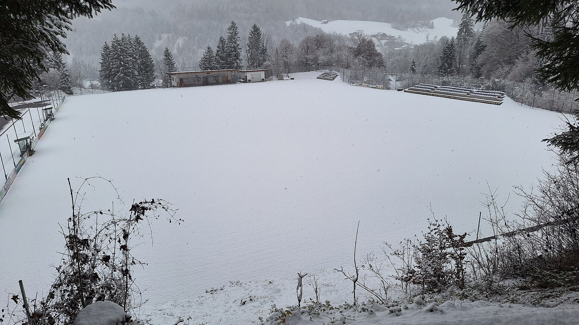 Verschneiter Sportplatz in Unken mit bewaldeten Hängen und einer verschneiten Wiese im Hintergrund