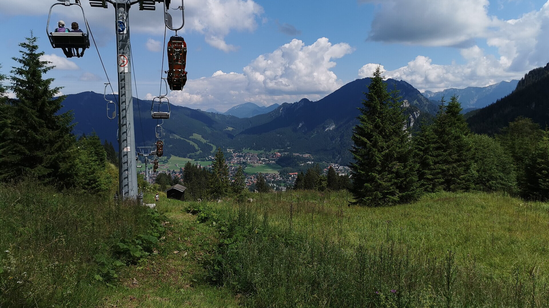 Sesselbahn am Kolbensattel oberhalb von Oberammergau im Sommer, dahinter der Ort und die Ammergauer Alpen