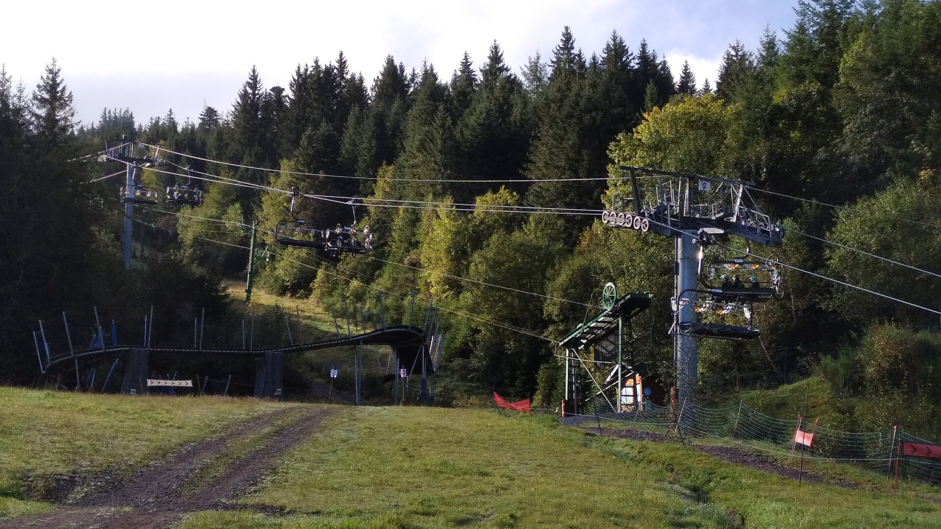 The Lac Blanc 900 base area in summer, a chairlift climbing a green slope between fir trees