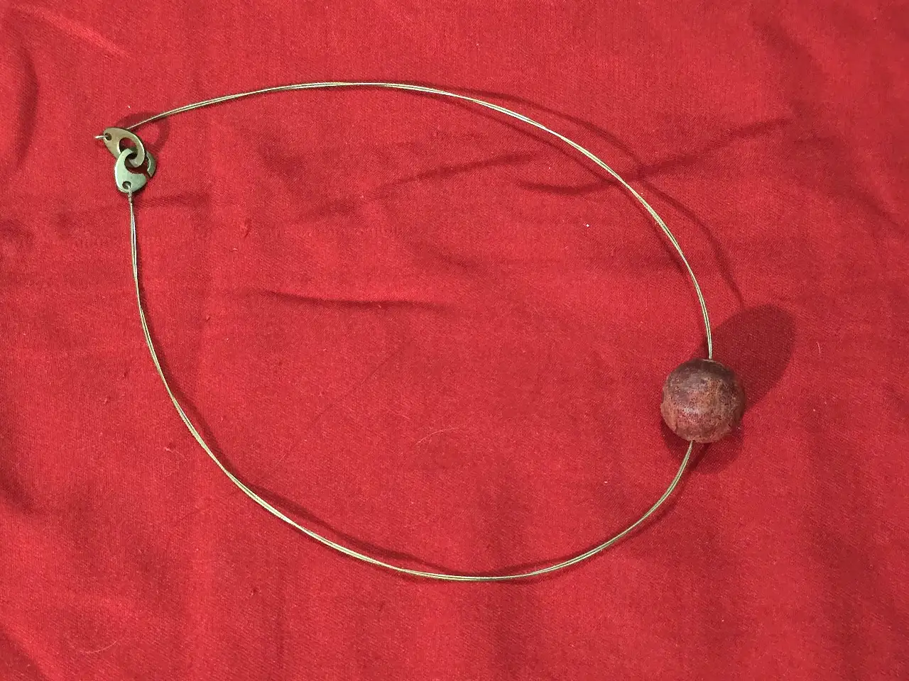 שרשרת קולר בעלת עיצוב מנימליסטי המורכבת מחישוק מתכת דק וחרוז מרכזי בגוון אדום