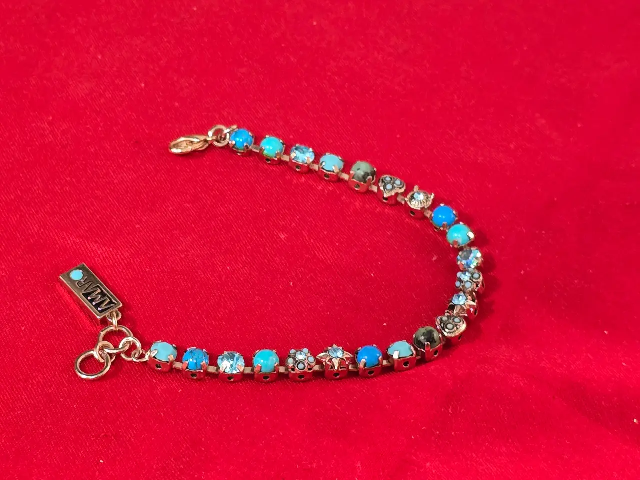 צמיד טניס וינט'ג של המותג אמארו (Amaro) עשוי מפליז בגימור מוזהב ומשובץ באבני תורכיז וקריסטלים בגווני כחול ותכלת