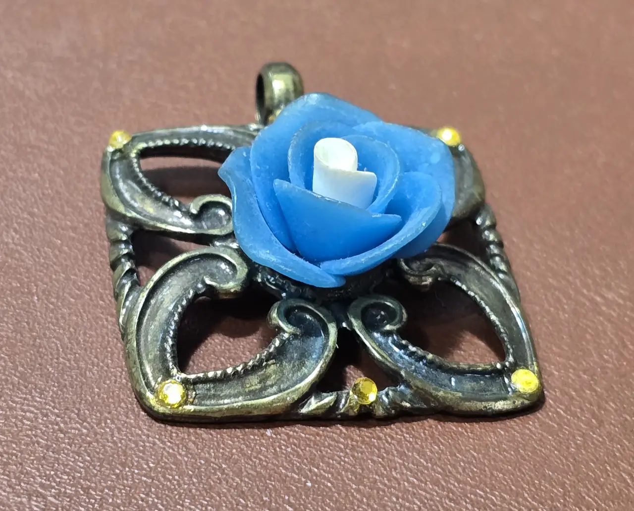 תליון מתכת כנראה ברונזה במרכזו שושנה כחולה התליוןל של ח'ב אבגד חברה ישראלית מידות 3.5*3