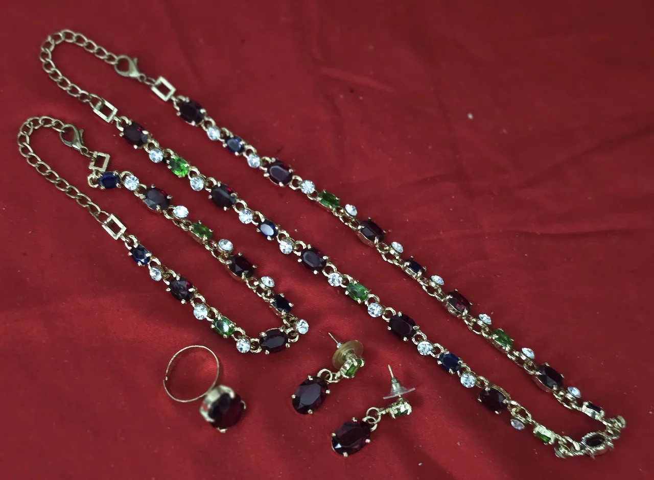 סט תכשיטים תואם בעל מראה קלאסי הכולל ארבעה פריטים 1- שרשרת ארוכה המורכבת מחוליות משובצות אבנים צבעוניות 2- צמיד תואם בעיצובו לשרשרת 3- עגילים זוג עגילי תליון 4- טבעת עם אבן מרכזית גדולה ובולטת האבנים בתחשיט הם רובי אמרלד גארנט ספיר קריסטלים וזרקונים המתכת ציפוי זהב