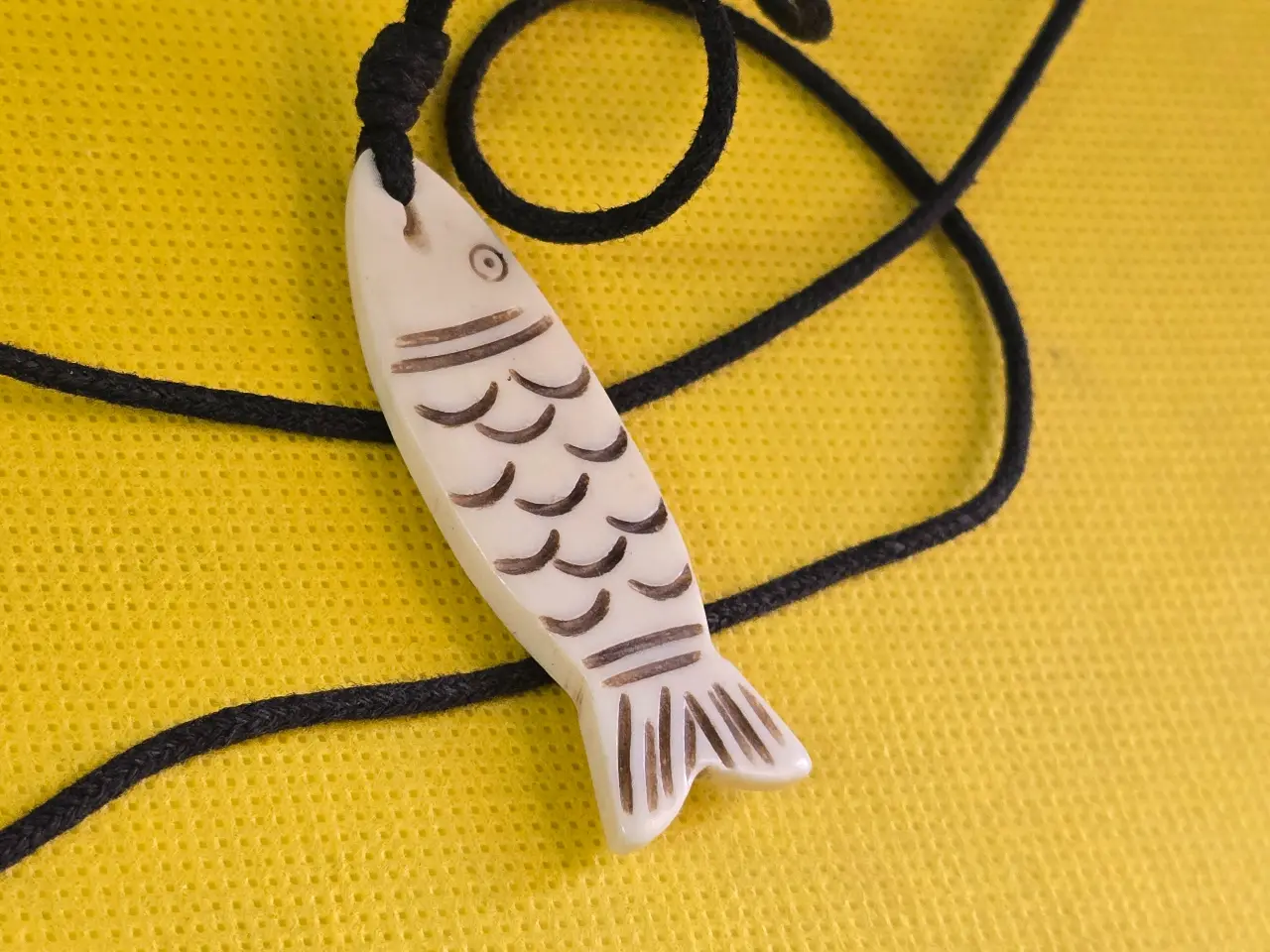 תליון דג נגד עין הרע, מגולף מעצם טבעית בעבודת יד, עם חוט שחור עבה.   מידות התליון - 5.5X1.8 סמ