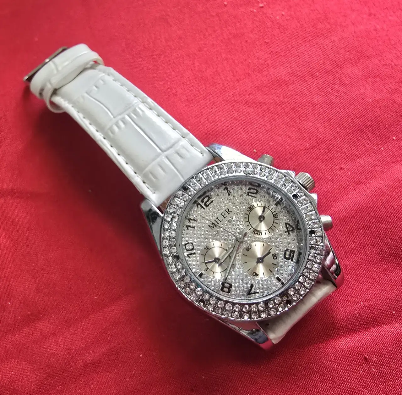 שעון יד חדש לגמרי הלוח מעוטר בשיבוץ צפוף של אבנים קטנות השעון עשוי ממתכת בגוון כסף רצועת עור לבנה דמוי עור תנין