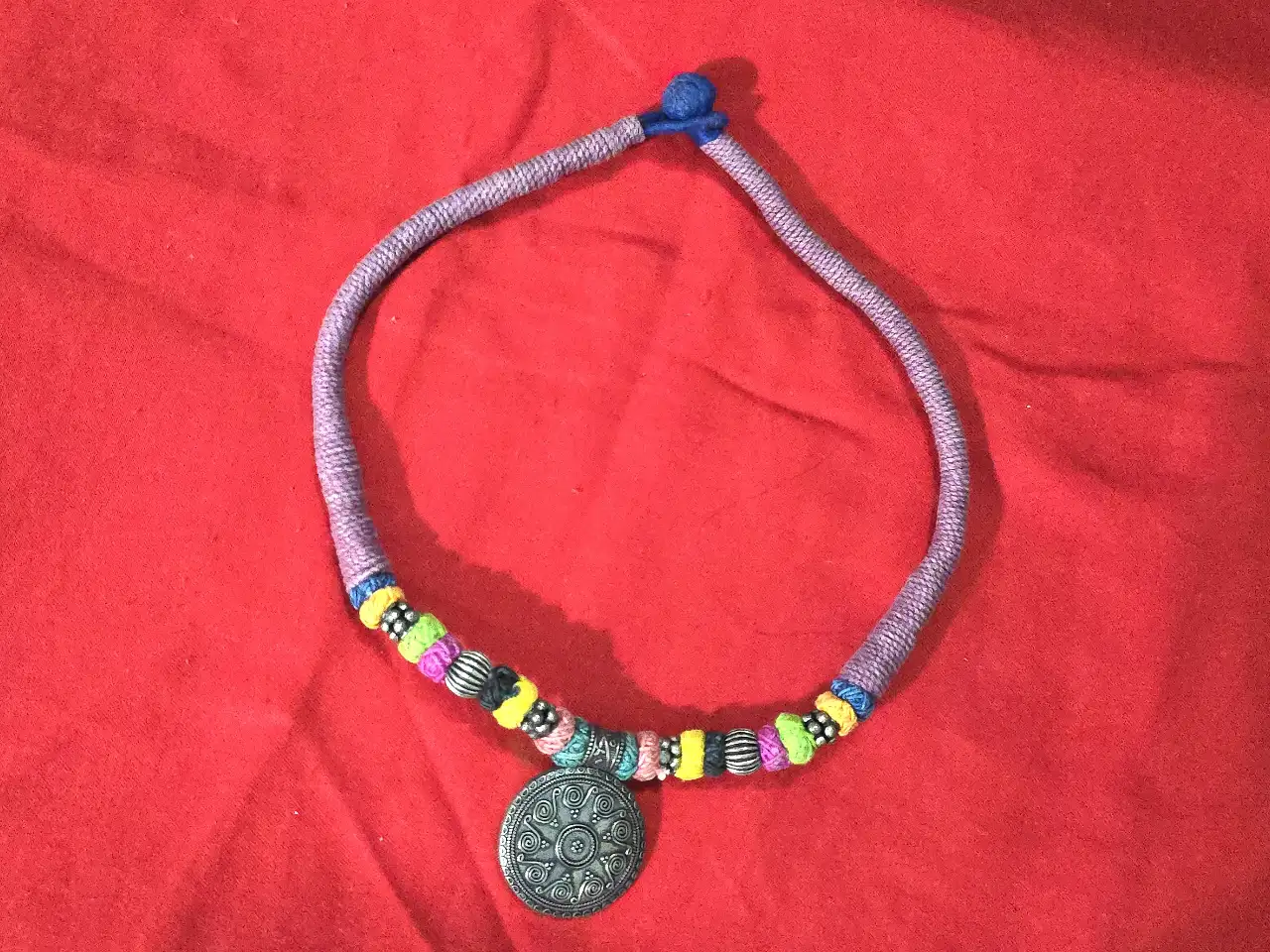 שרשרת בסגנון אתני\שבטי השרשרת עשויה מחבל או חוט כותנה עבה עטוף בליפוף של חוטים צבעוניים משולבים בה חרוזי מתכת ותליון מתכת במרכז בעיצוב עתיק