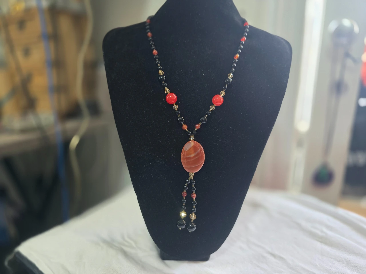 שרשרת ארוכה הכוללת תליון אבן מרכזי השרשרת משלבת אבני קרנליאן כתומות ואדומות עם אבני אוניקס שחורות