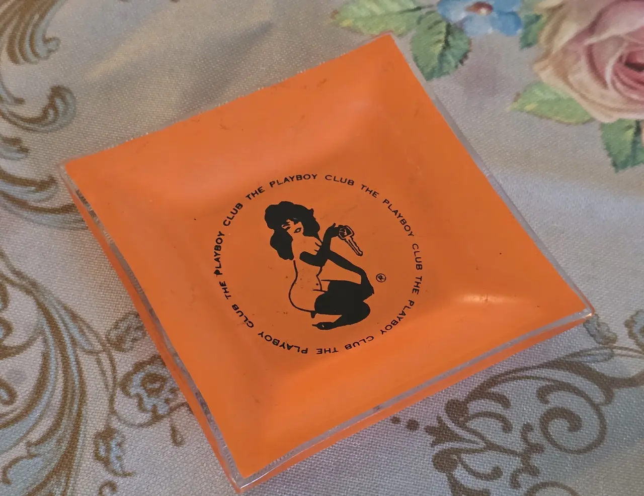 מאפרת זכוכית כתומה וינטג' "The Playboy Club", הדפס דמות ארנבונת המחזיקה מפתח – פריט אספנות רטרו מידות: 9.5 x 9.5 ס"מ