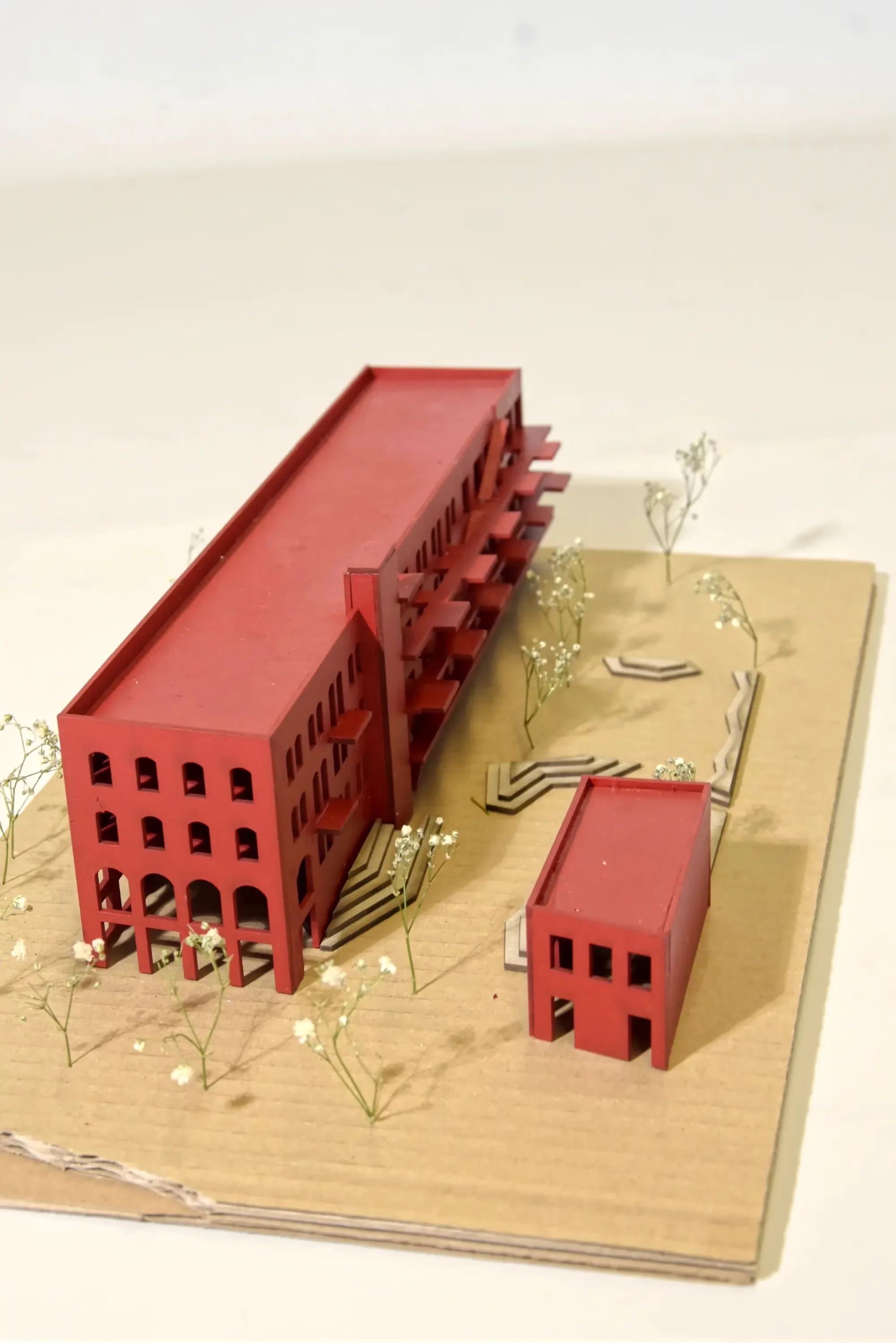 Vogelperspektive auf das rote Modell: Die Rückseite des Hauptgebäudes zeigt auskragende Laubengänge; davor ein kleinerer roter Neubau.