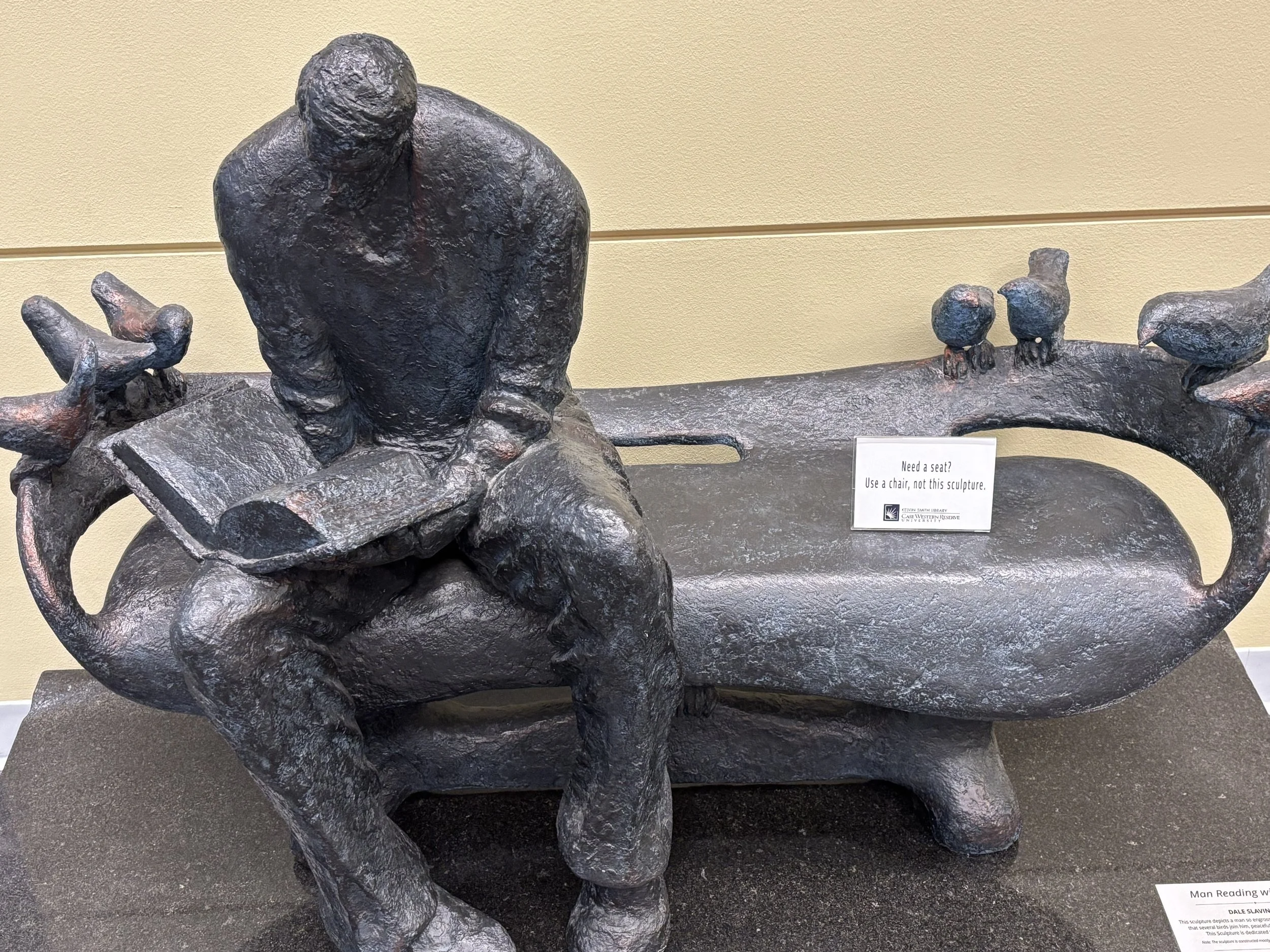 A statue depicting a man sitting on a bench at Case Western Reserve University library