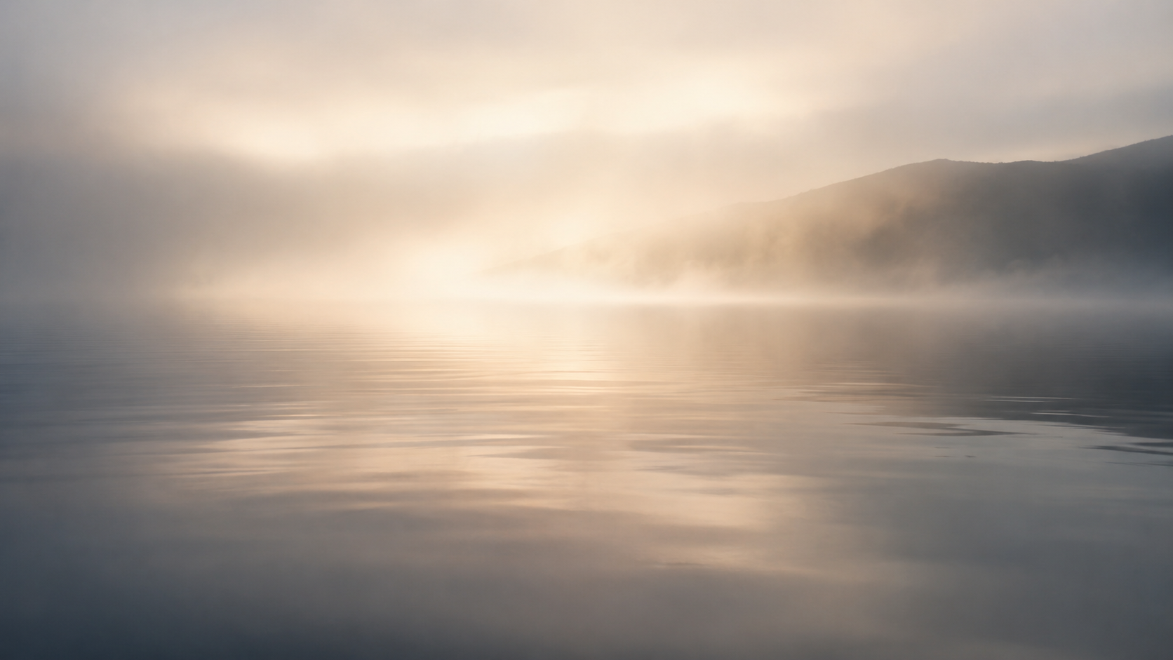 Calm water with subtle ripples beneath a softly glowing misty horizon, with faint distant land at the right.