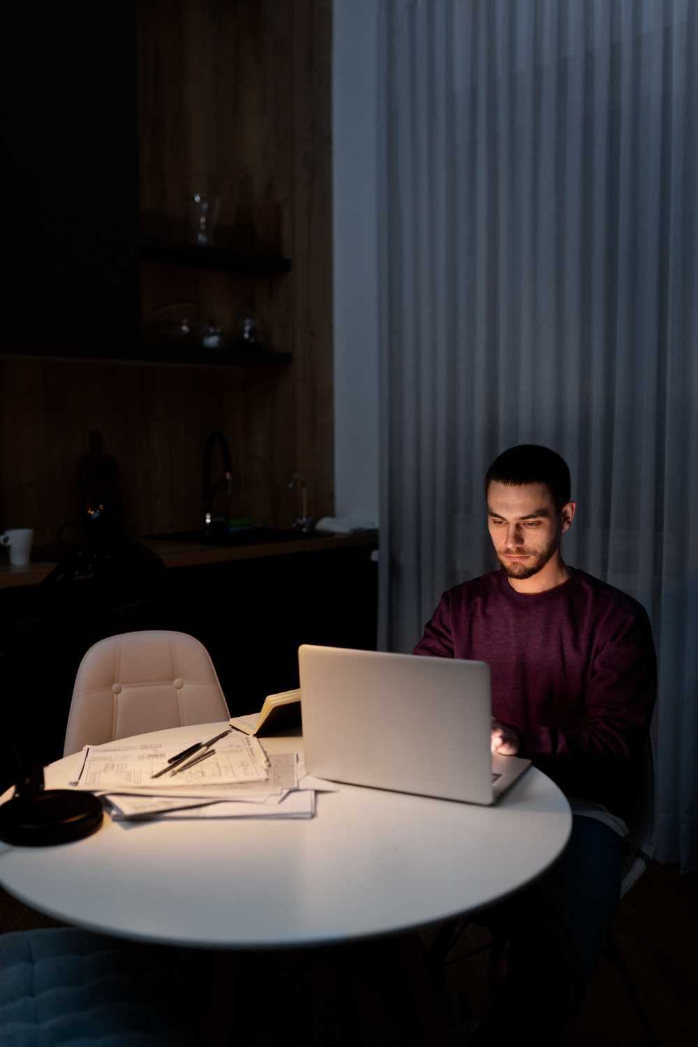 Young man squinting at a laptop screen in a dimly lit room.