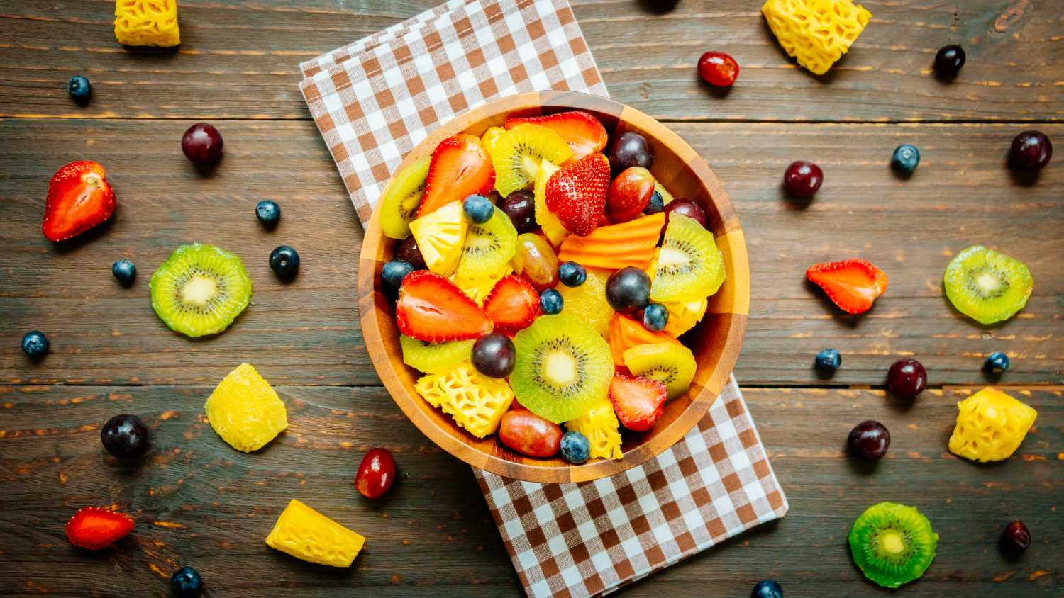 A bowl of colorful fruits, nuts, and leafy greens on a wooden table.