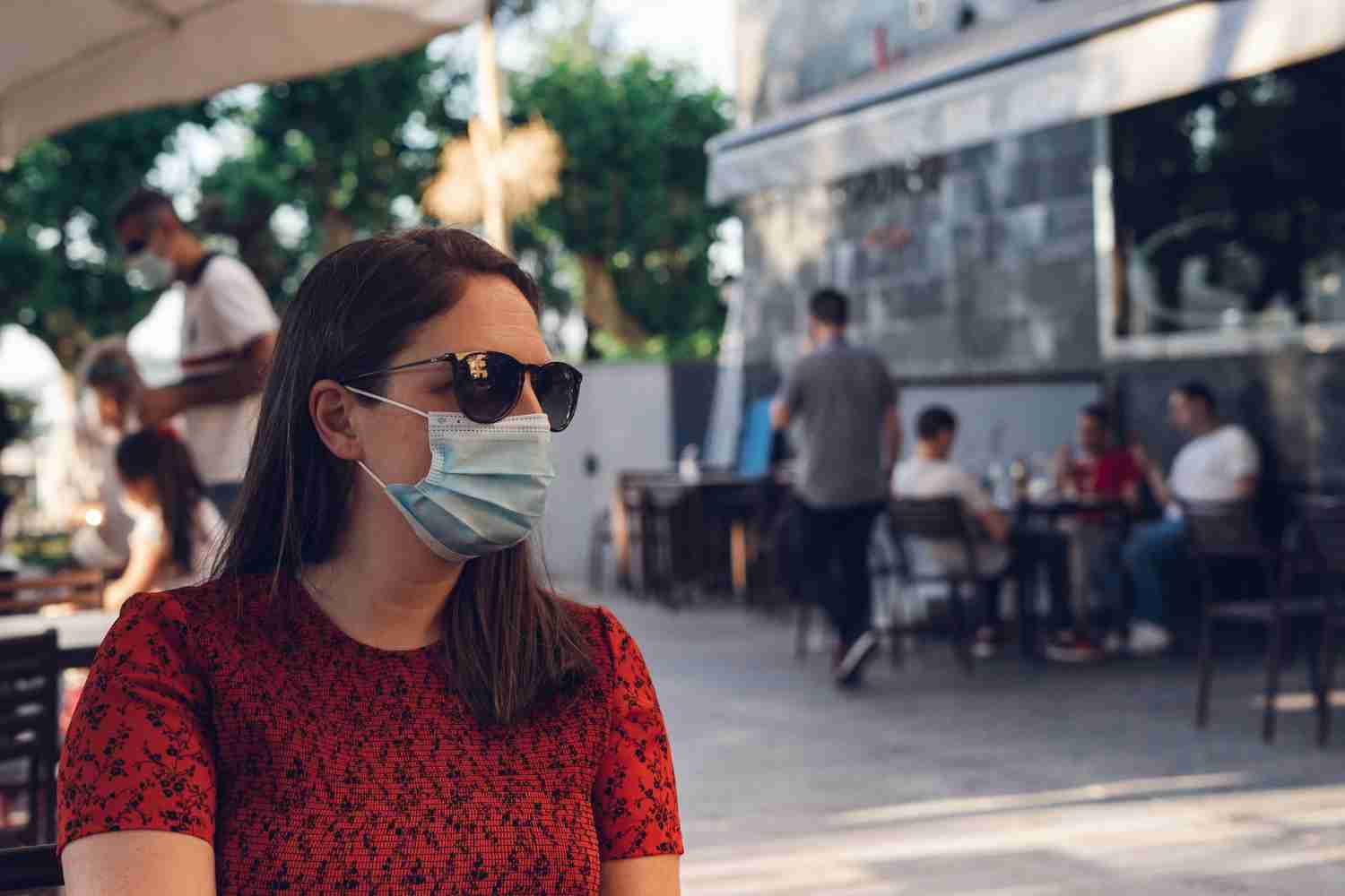  A woman wearing a face mask in a public space, with blurred crowds in the background.